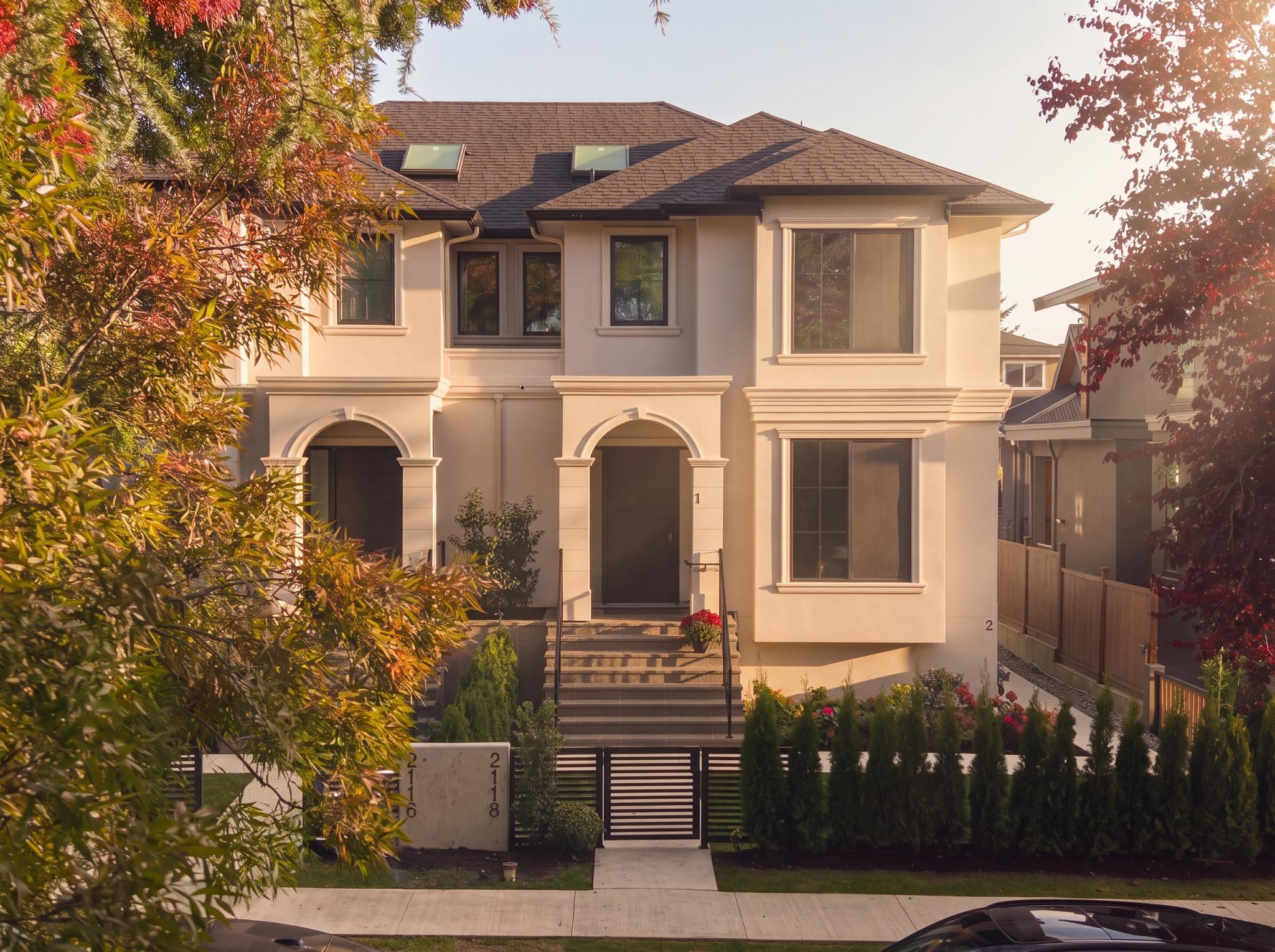 Two-storey cream home with arched entryways and front steps, framed by colorful autumn trees.