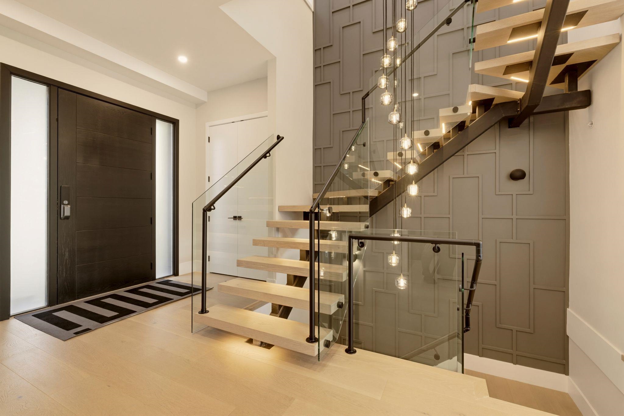 Modern entryway with a floating wood staircase, glass railings, and hanging pendant lights.
