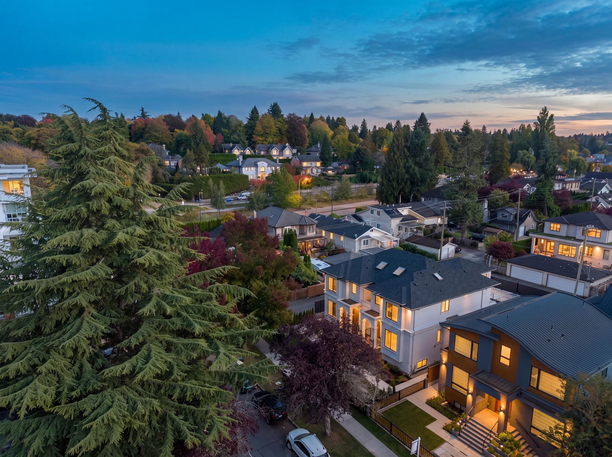 Aerial view of a tree-lined residential neighborhood at dusk, with illuminated homes and autumn foliage.