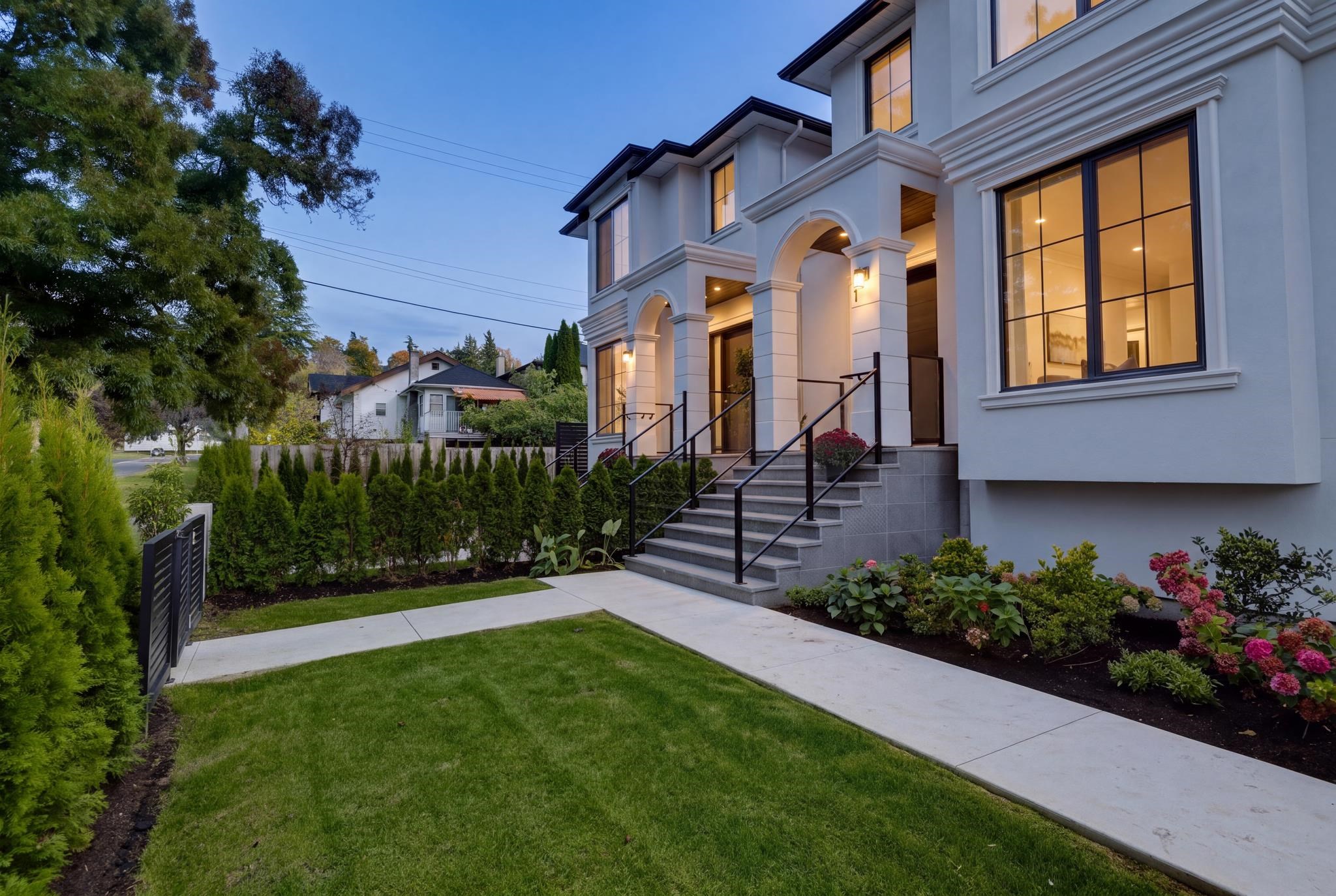 Multi-story home with arched entryways, broad front steps, and landscaped front garden at dusk.
