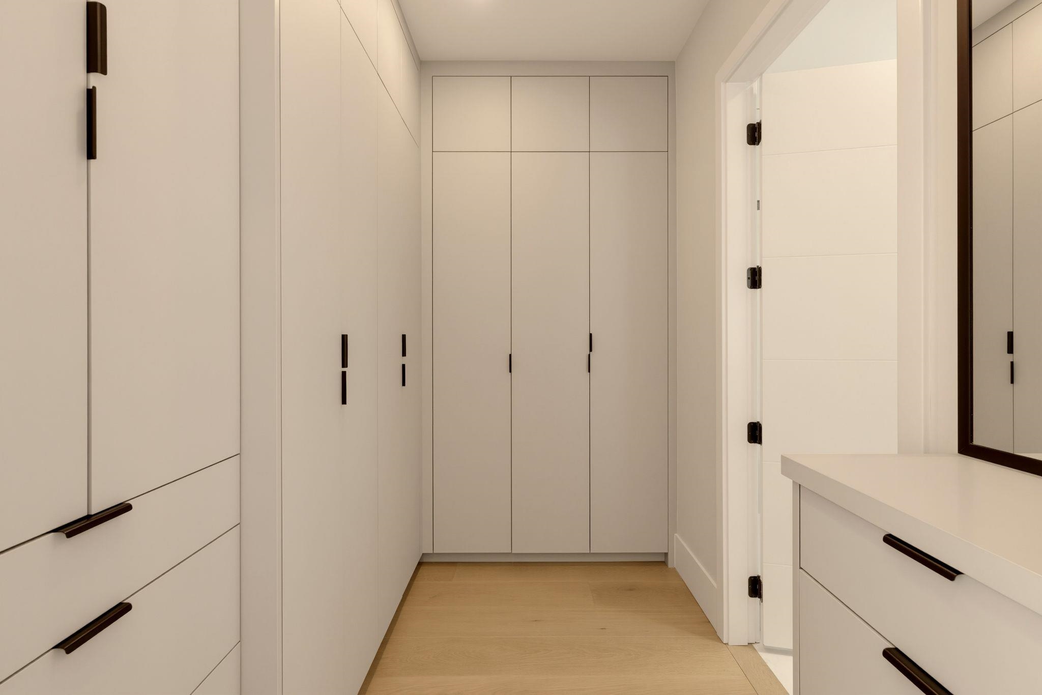 Walk-in closet with white built-in cabinetry, black handles, and light wood flooring.