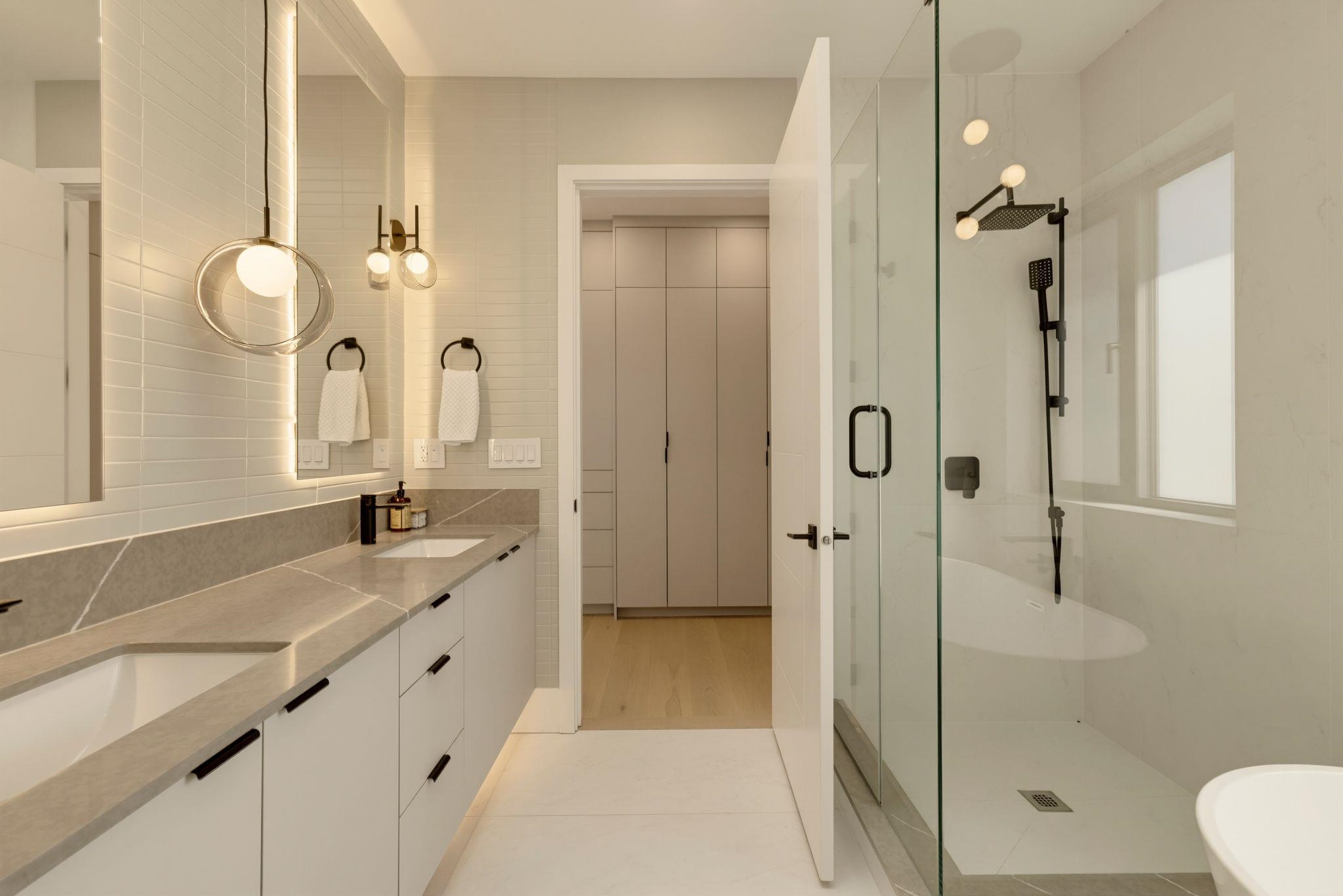 Modern bathroom with a long double vanity, glass walk-in shower, and partial view of a freestanding tub.