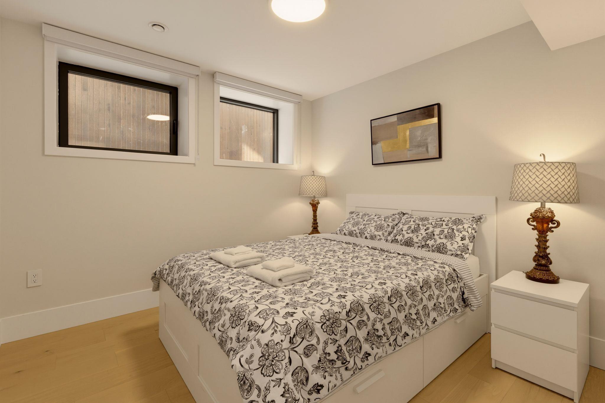 Bedroom with a white bed, floral bedding, matching bedside lamps, and high windows.