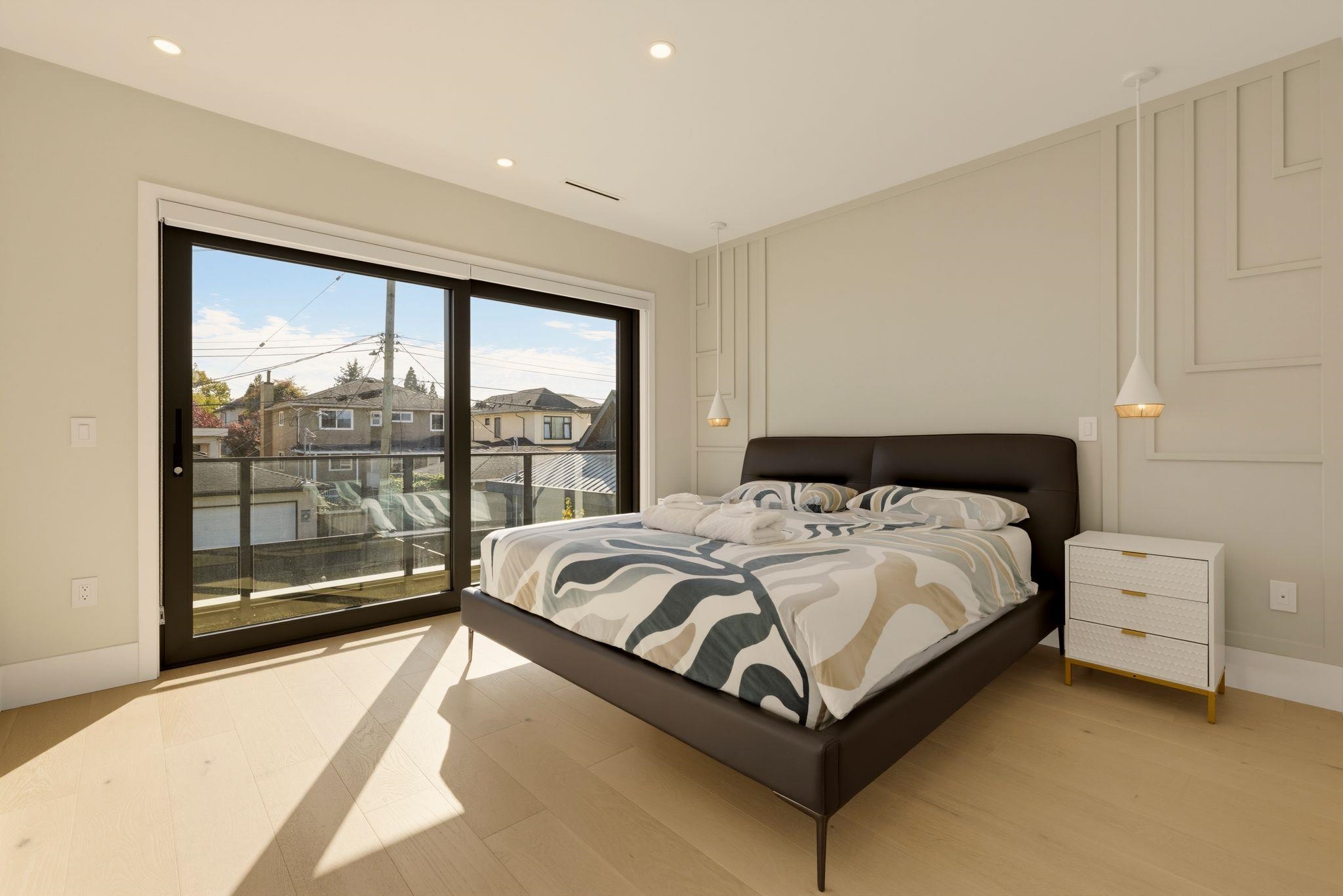 Bedroom with a dark bed and patterned bedding beside sunlit sliding glass doors.