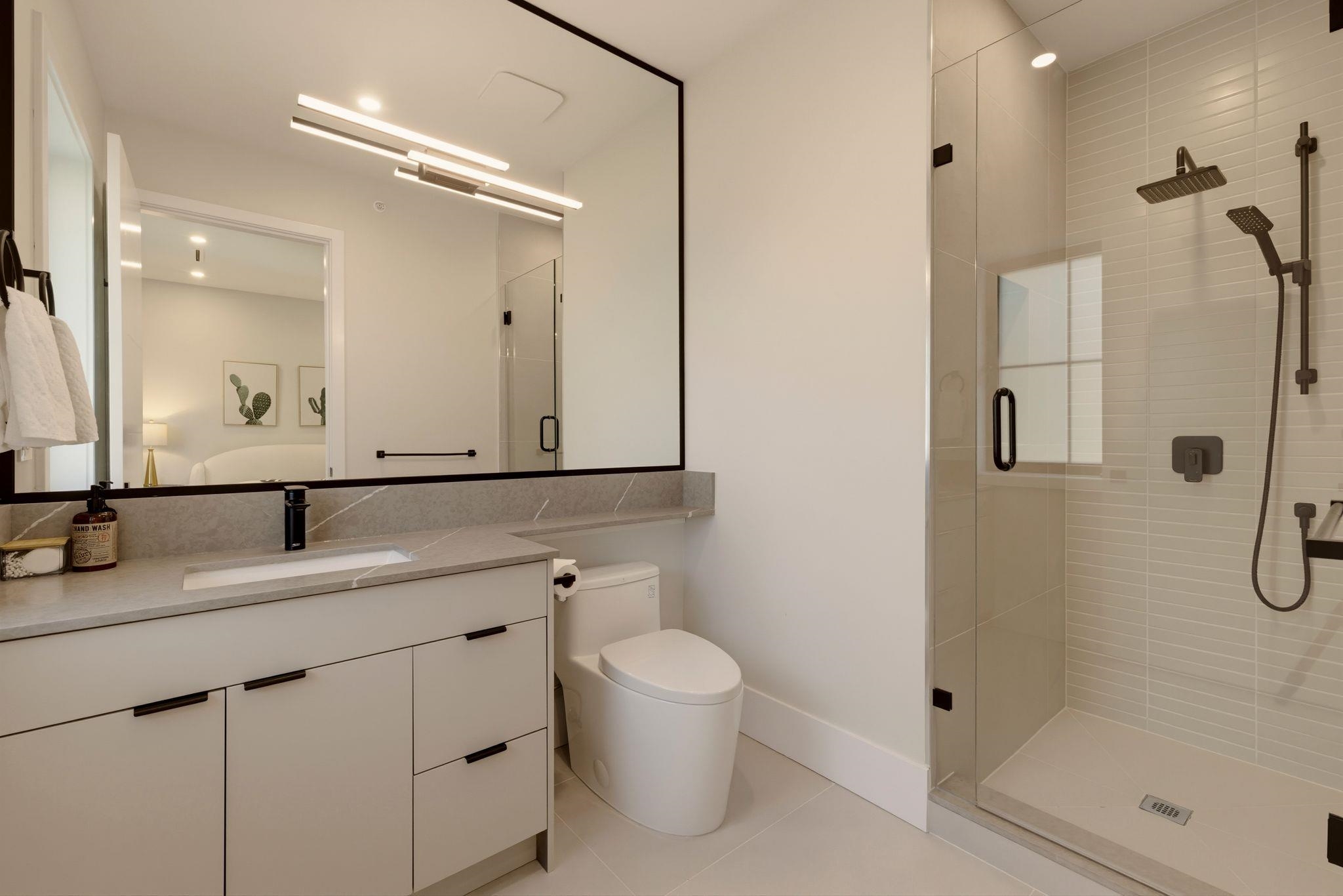 Modern bathroom with a floating vanity and black-framed mirror beside a glass shower with dark fixtures.