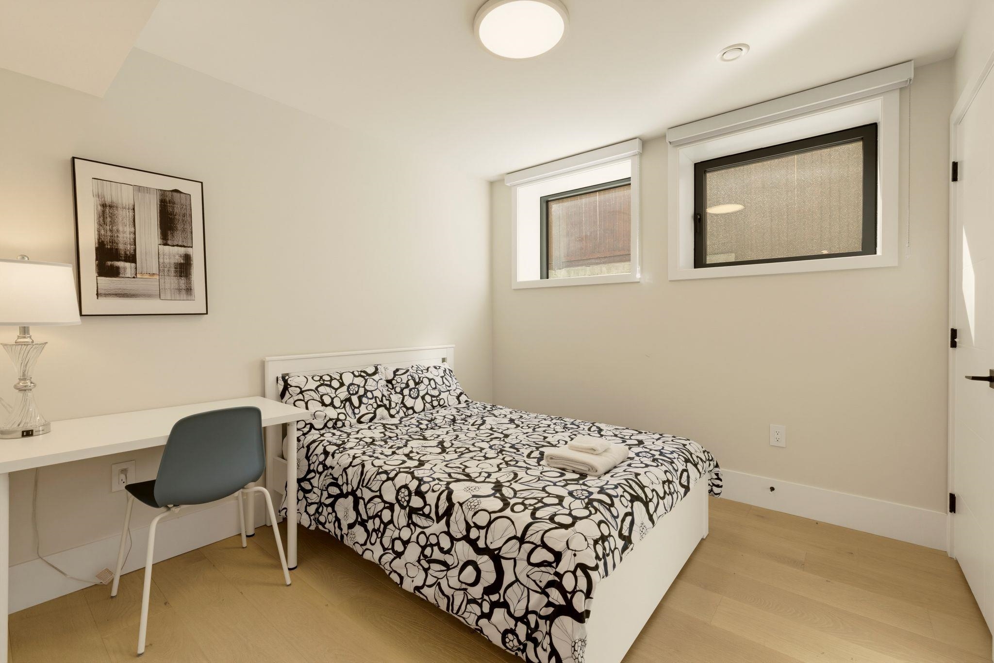 Bedroom with black-and-white floral bedding, a small desk, and two high windows.