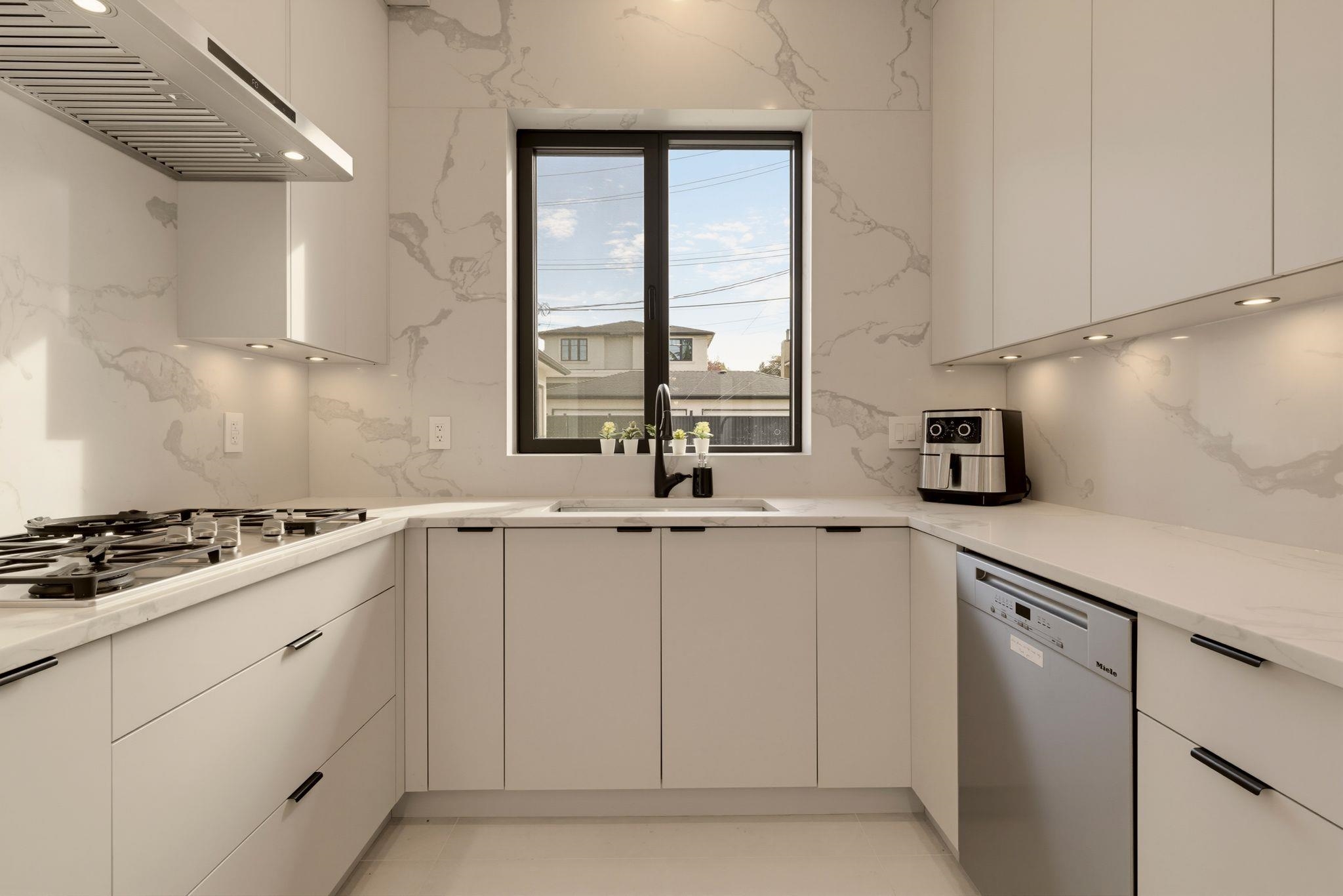 Modern white U-shaped kitchen with marble-look surfaces and a window above the sink.