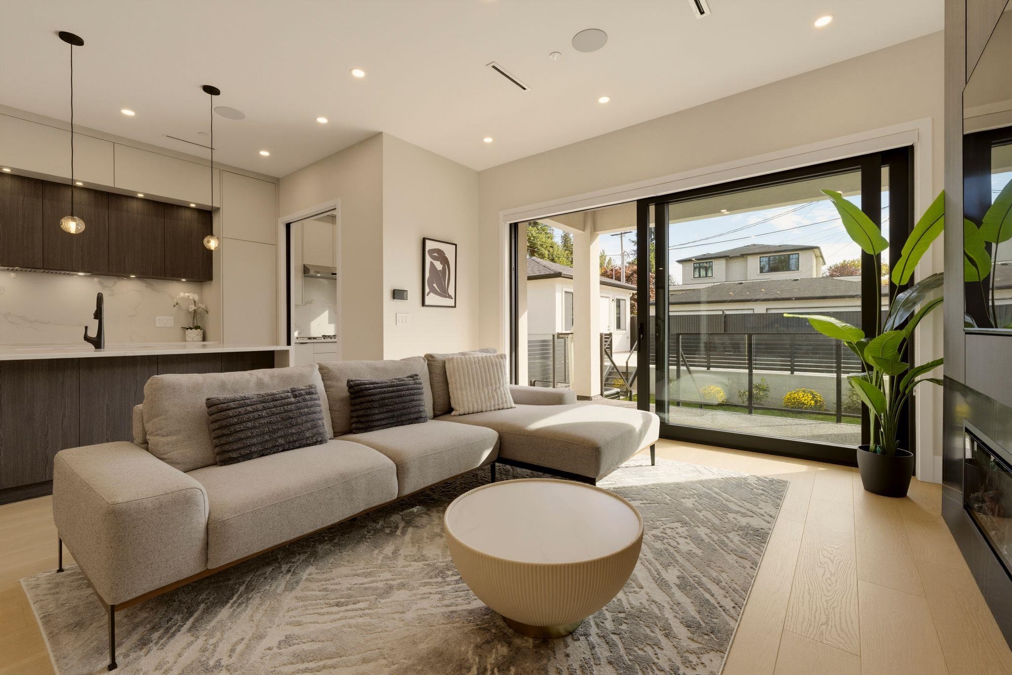 Modern living room with a beige sectional sofa and large glass doors opening to a fenced patio.
