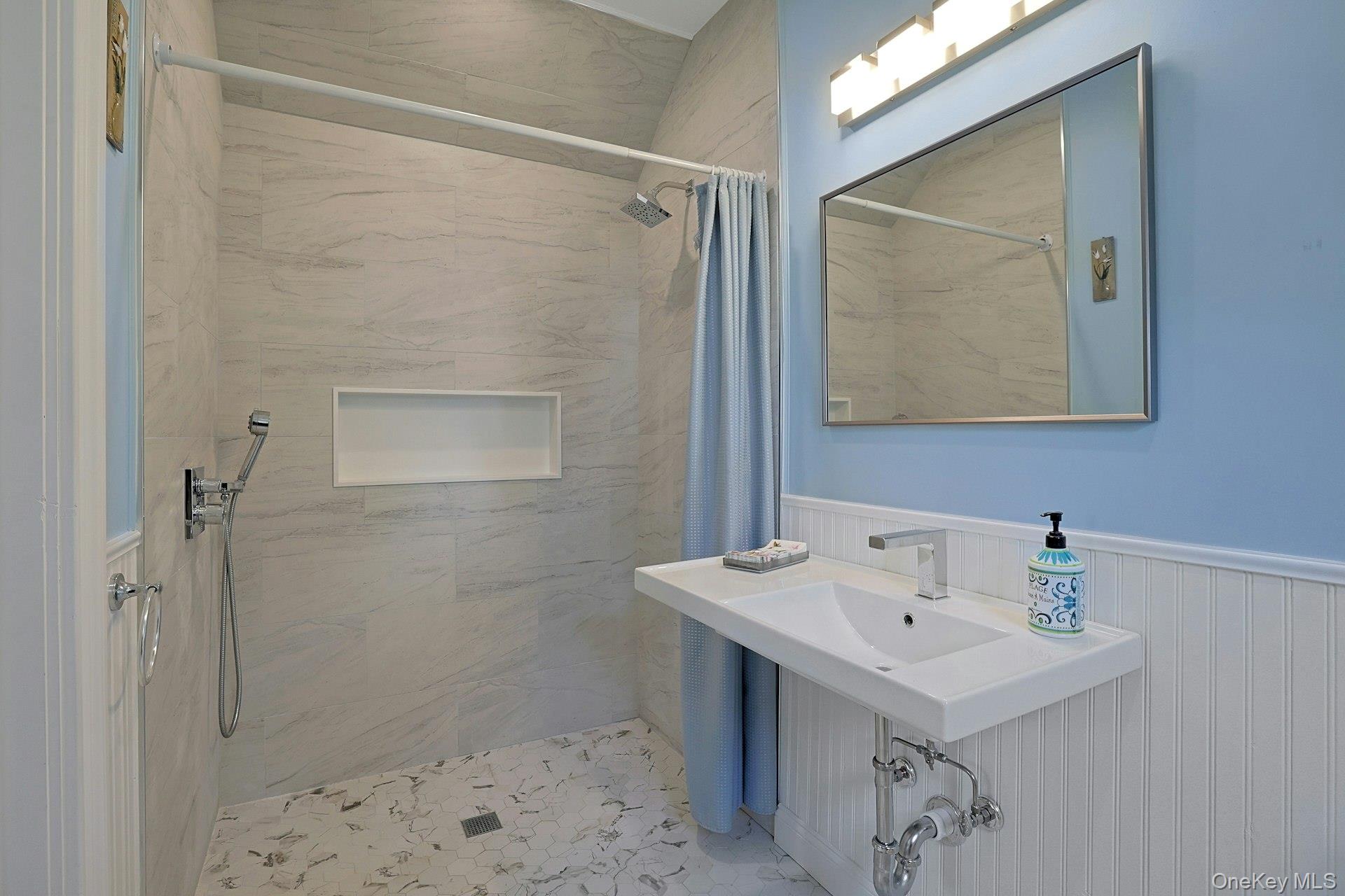 Bathroom with a marble-tiled walk-in shower, recessed niche, and white sink against blue walls.