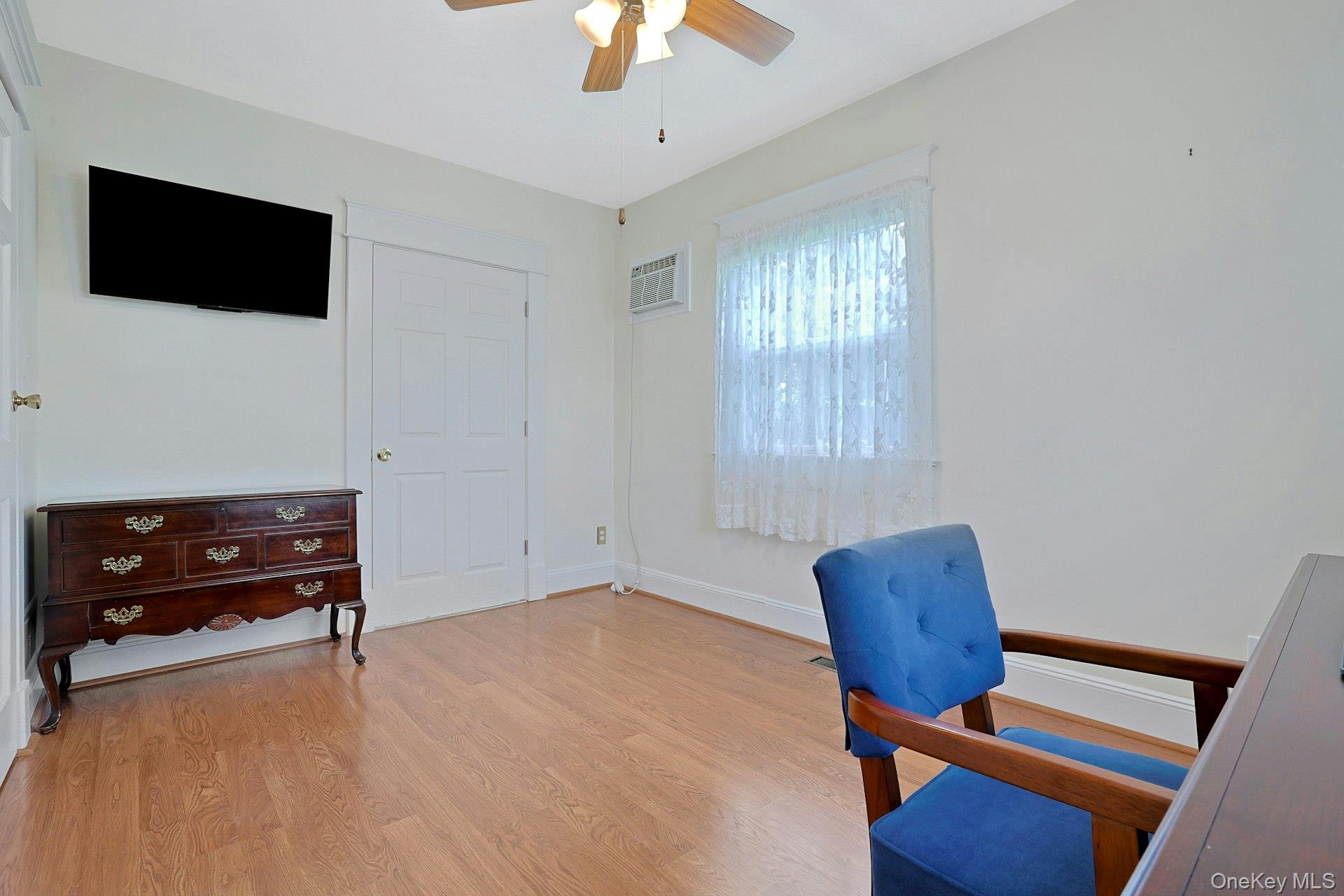 Furnished room with wood floors, a dark dresser, wall-mounted TV, and blue upholstered chair.