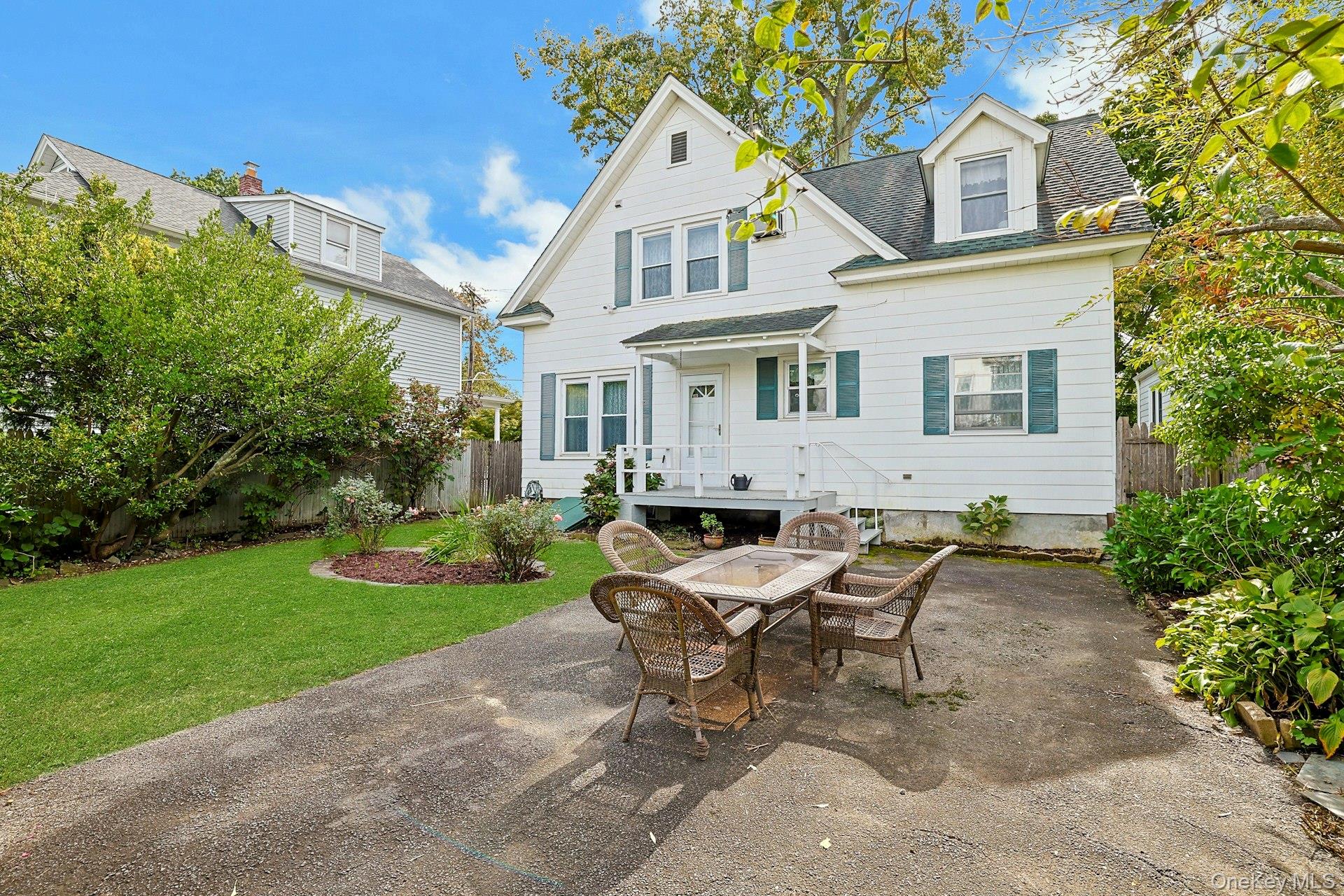 White two-story house with teal shutters, a small porch, and a wicker dining set on the backyard patio.