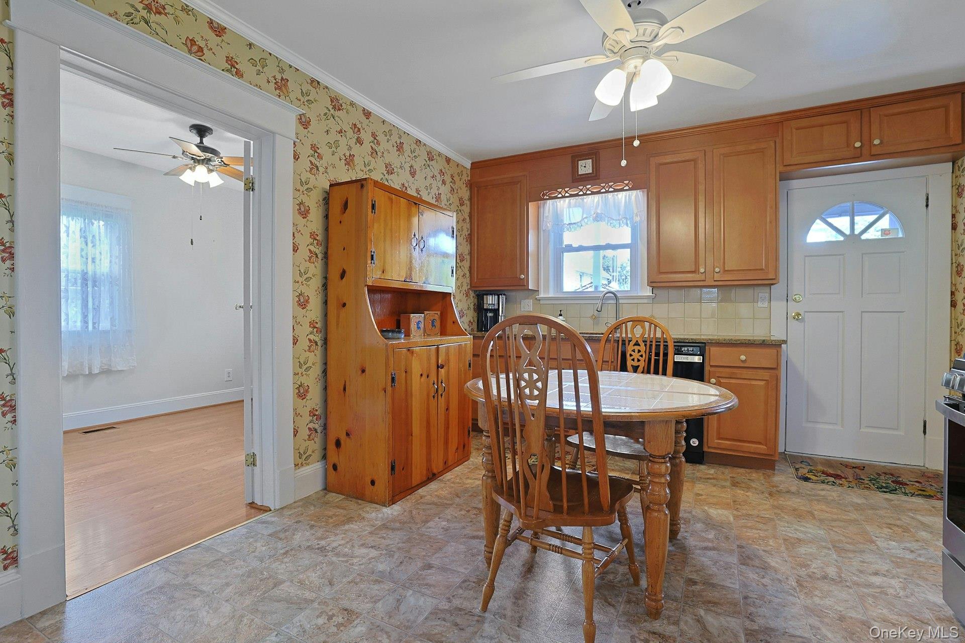 Kitchen and dining area with wood cabinetry, a round table, floral wallpaper, and tiled floors.