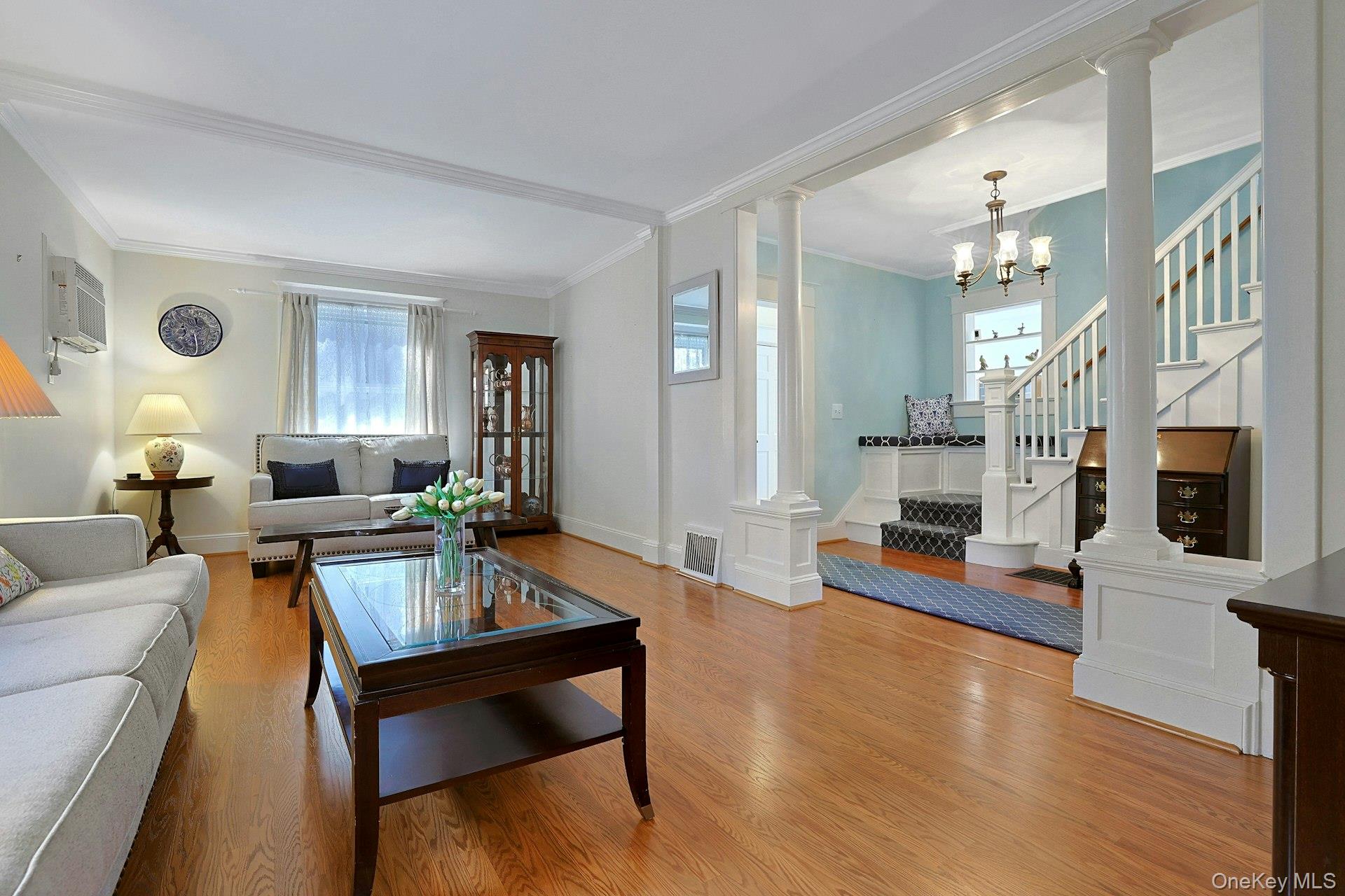 Living room with hardwood floors, white sofas, and a staircase against a blue accent wall.