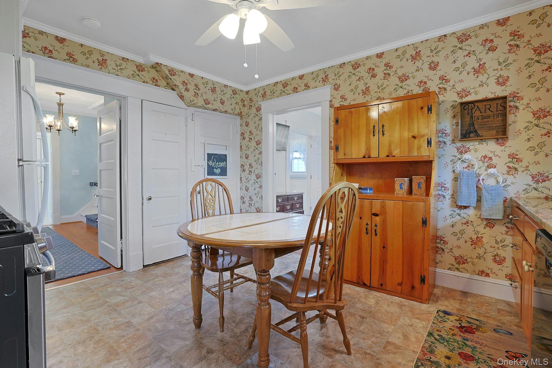 Kitchen and dining area with floral wallpaper, a wooden table, and a large pine hutch.