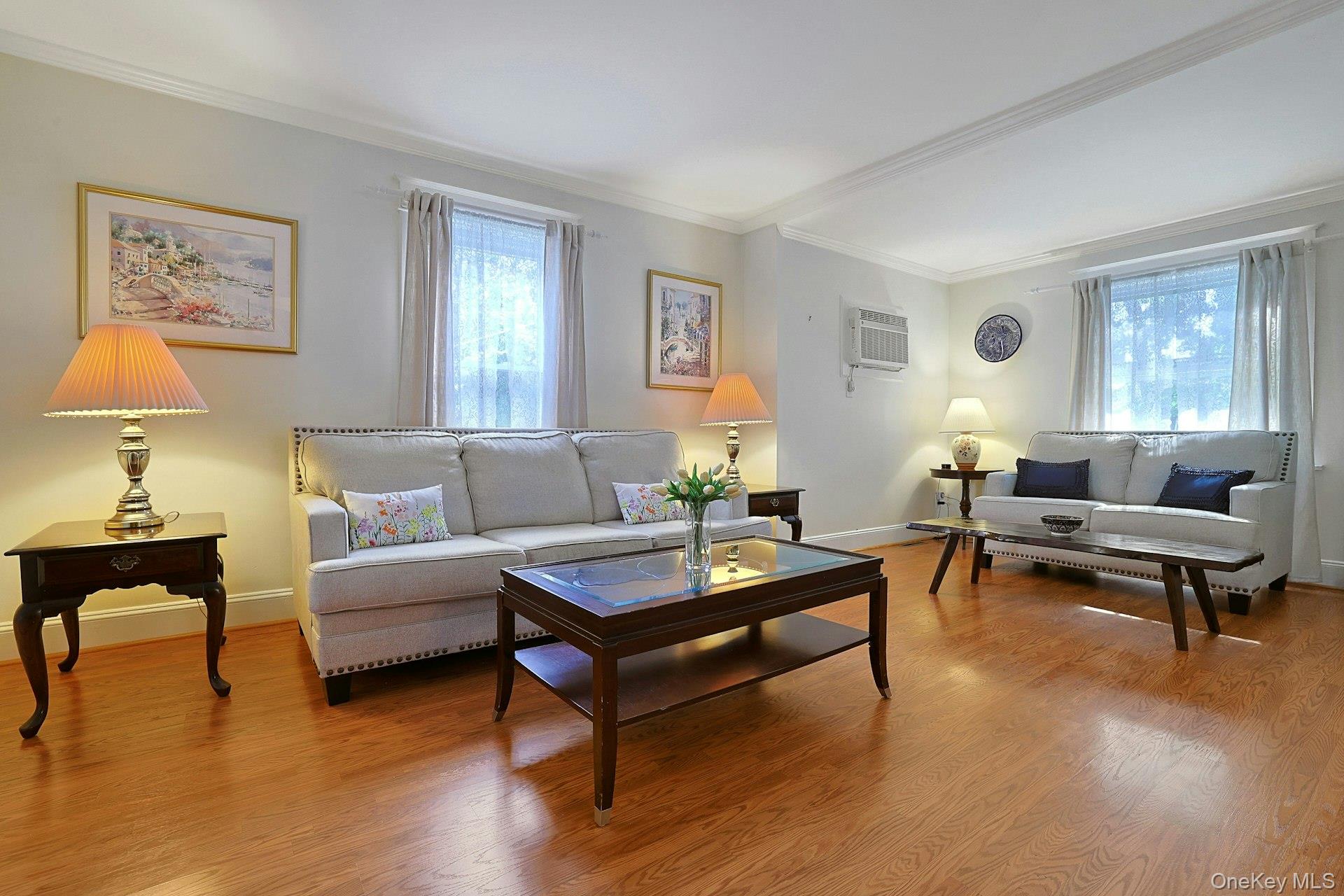 Living room with two light sofas, polished hardwood floors, and curtained windows.