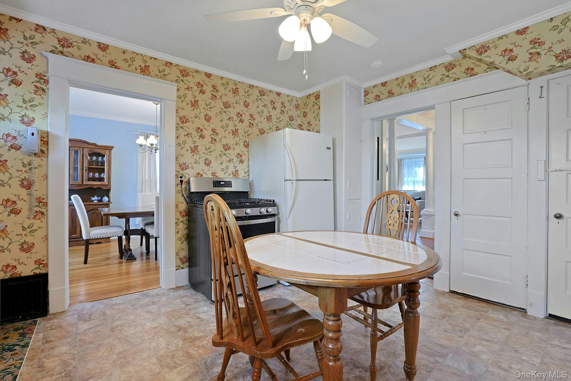 Kitchen with floral wallpaper, gas range, white refrigerator, and oval dining table.