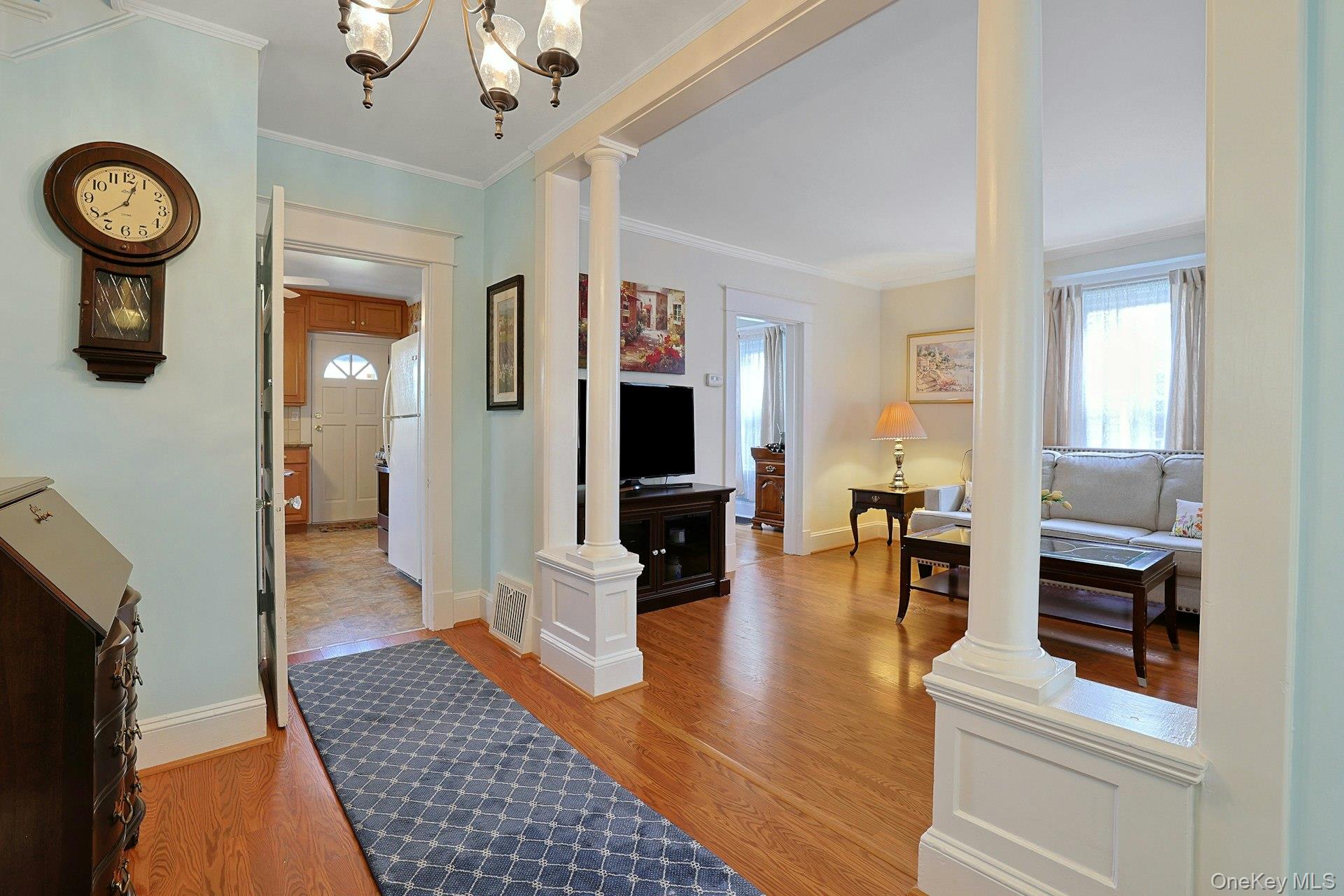 Open living room with white columns, hardwood floors, and a gray sofa.