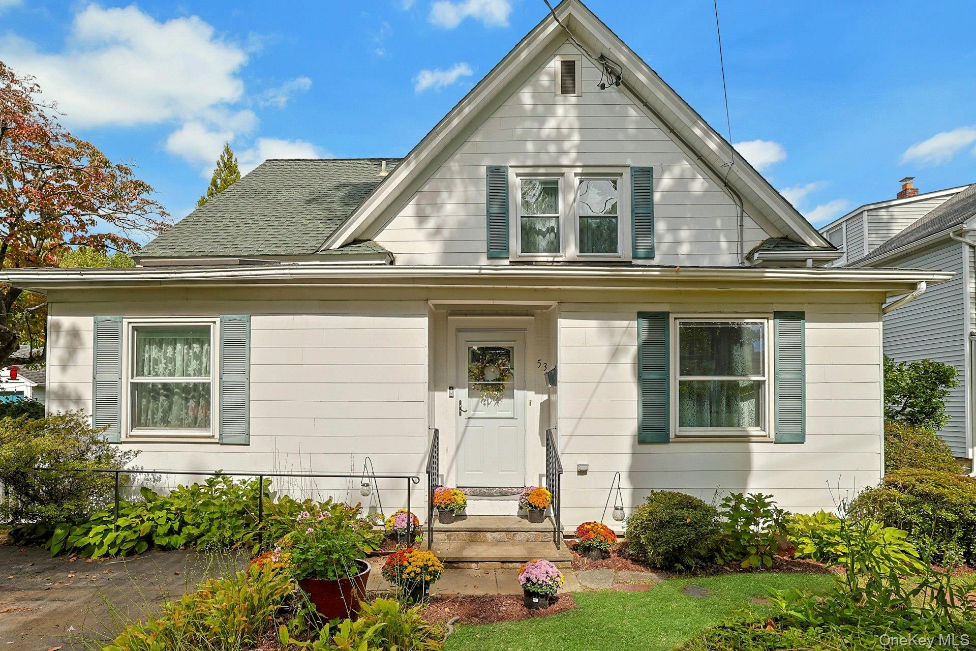 White gabled house with green shutters and flower pots beside the front walkway.
