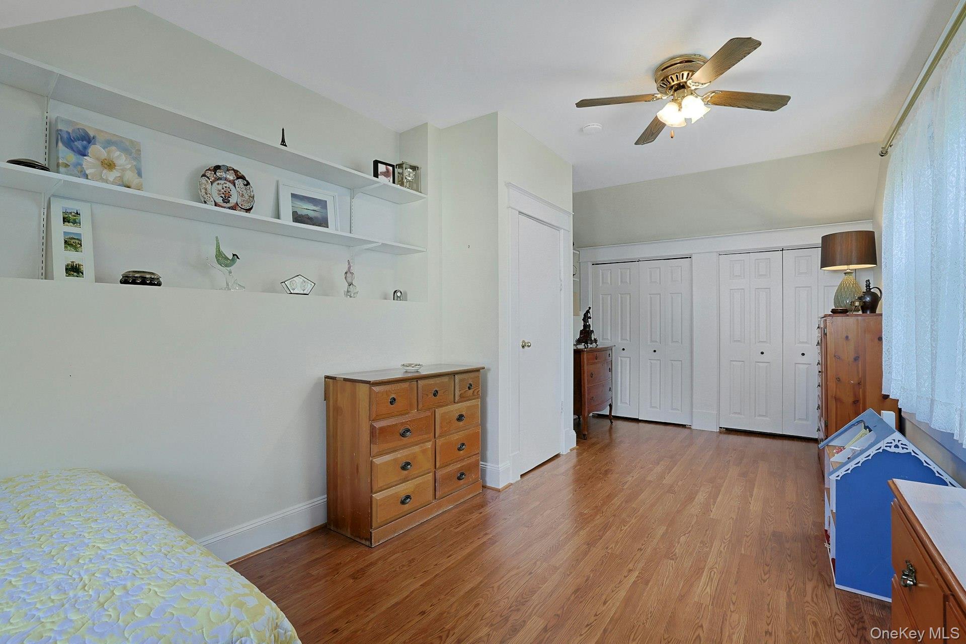 Bedroom with hardwood floors, built-in display shelves, and white closet doors.
