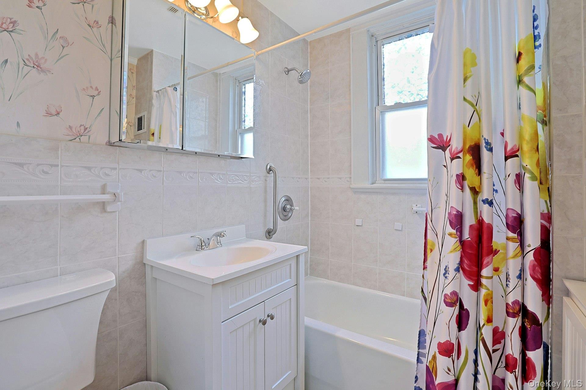 Bathroom with a white vanity and tub, tiled walls, and a colorful floral shower curtain.