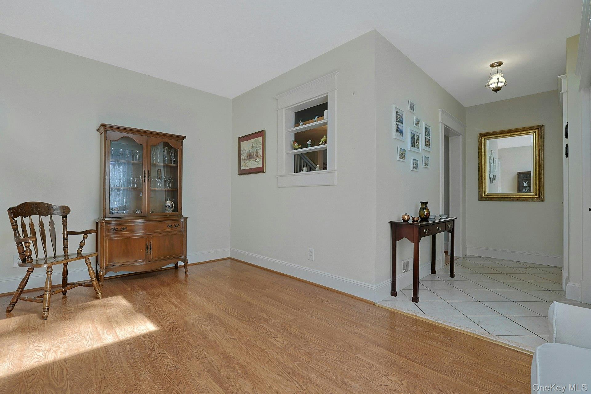 Living room with hardwood floors, a wooden display cabinet, and an opening to a tiled entry hall.