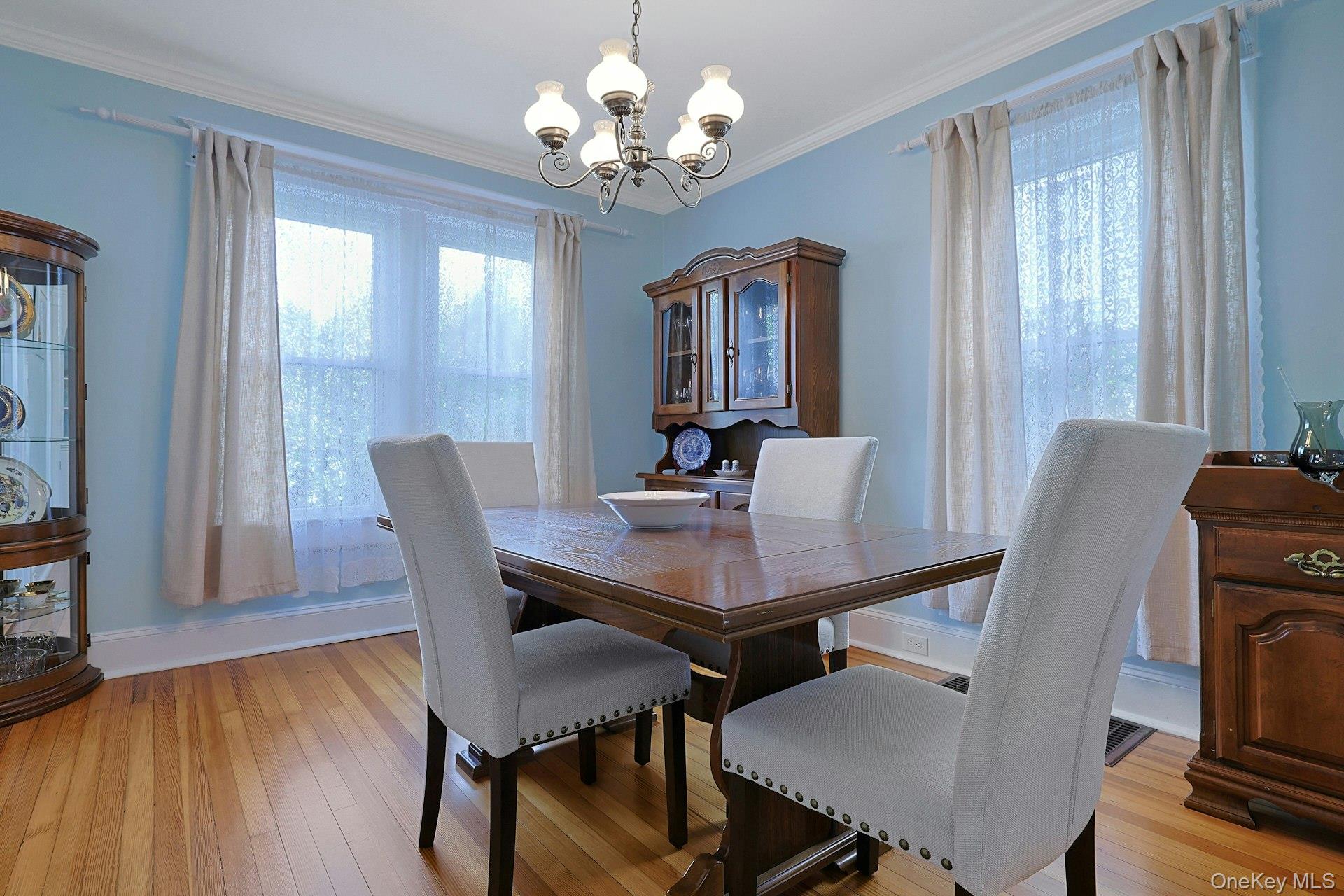 Dining room with a dark wood table, upholstered chairs, blue walls, and lace-curtained windows.