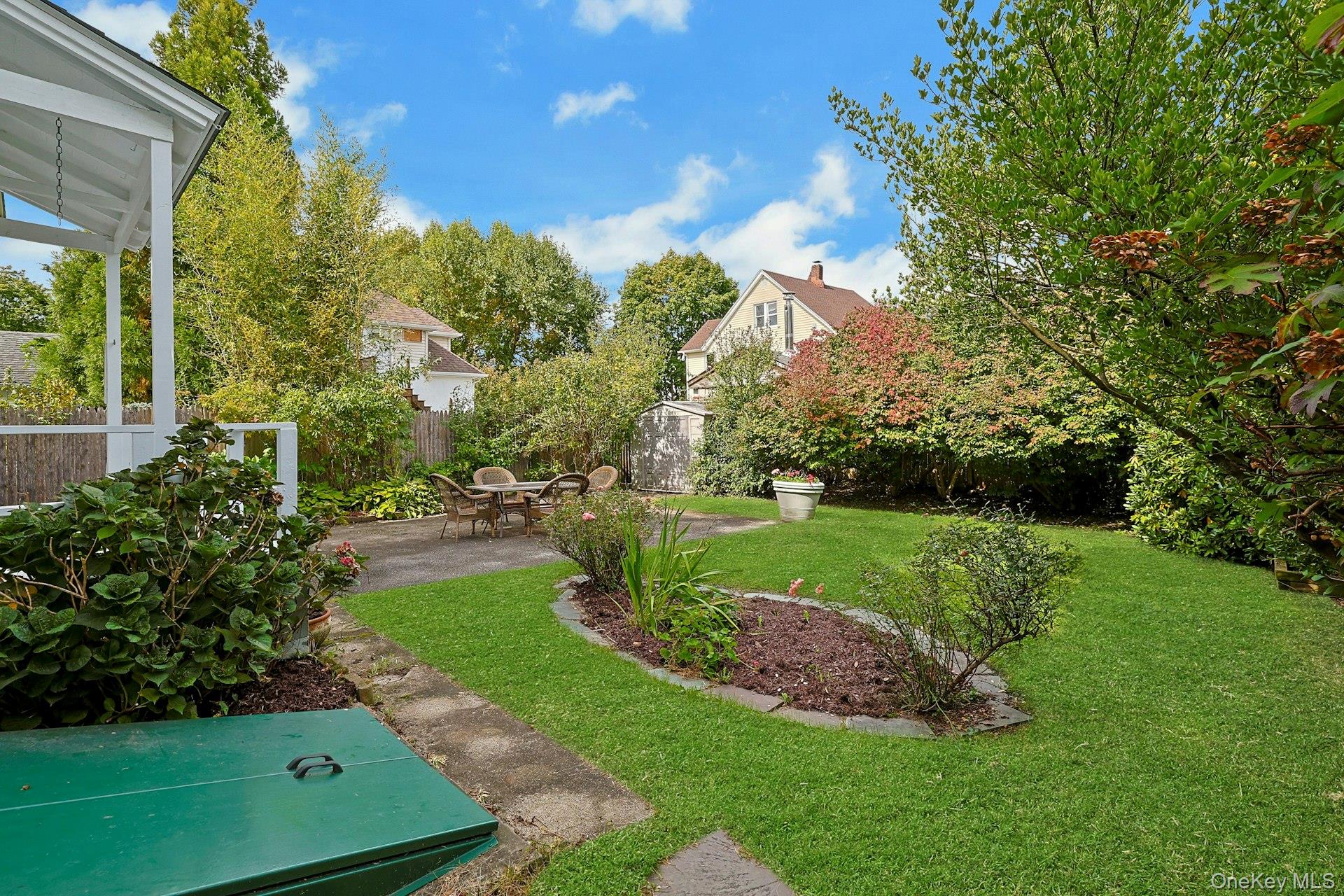 Backyard with a paved patio, outdoor dining set, garden beds, and a covered porch.