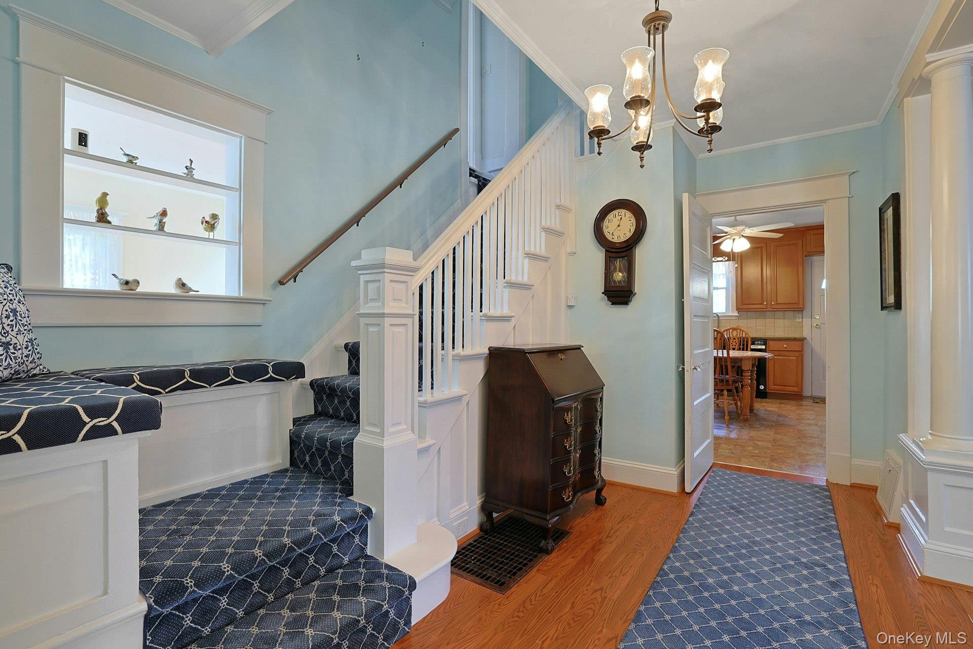 Entry hall with a carpeted staircase, built-in window seat, and doorway to the kitchen.