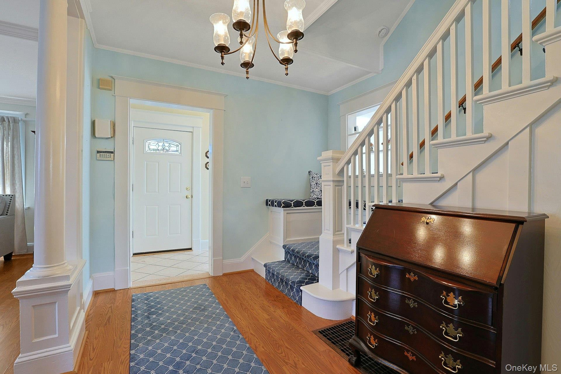 Entry hall with a white staircase, blue patterned carpet, hardwood floors, and a dark wooden chest.