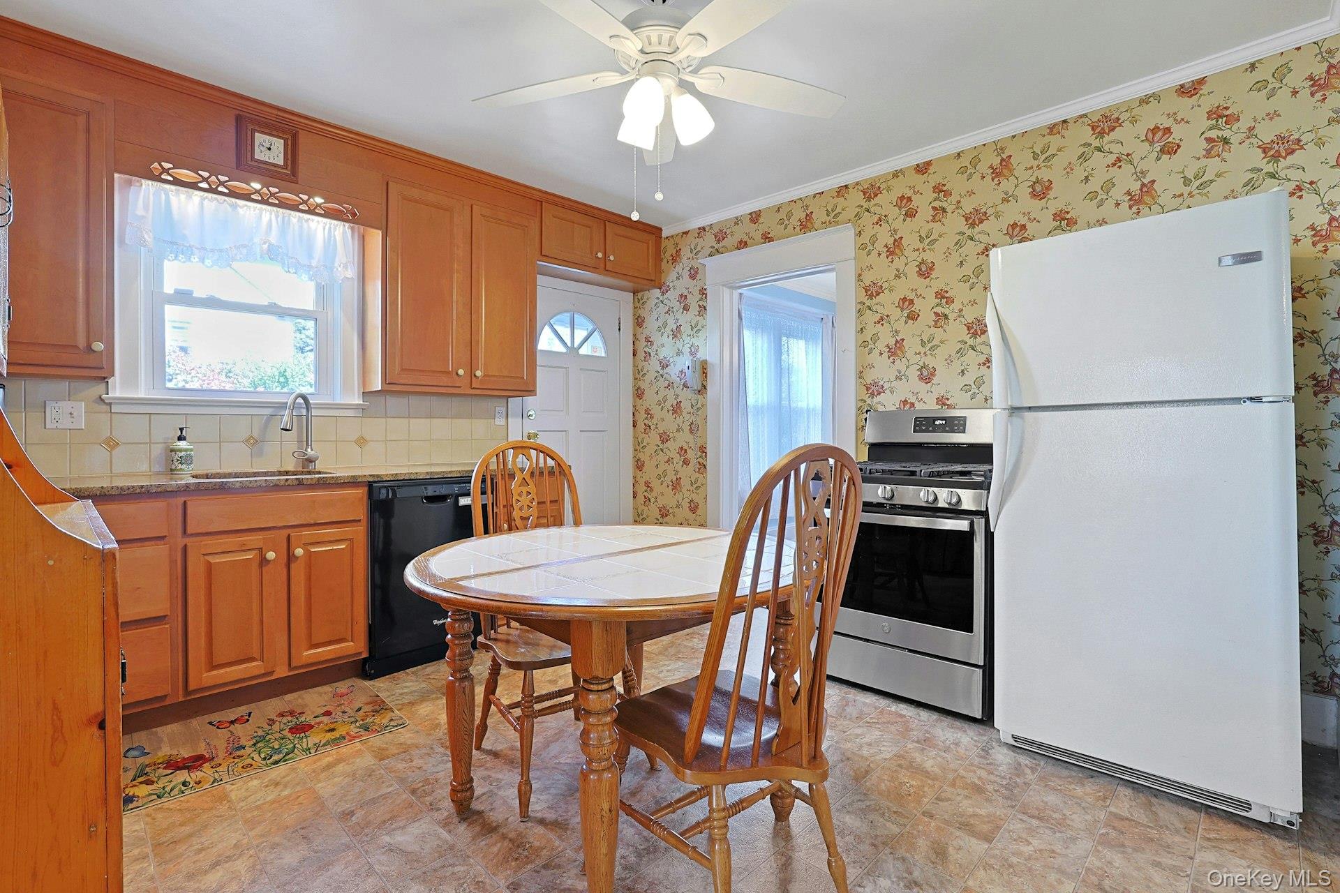 Kitchen with wood cabinets, floral wallpaper, and a dining table beside a white refrigerator.
