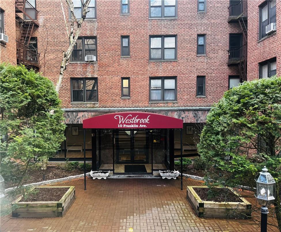 Red-brick apartment building entrance with a Westbrook awning and landscaped brick courtyard.