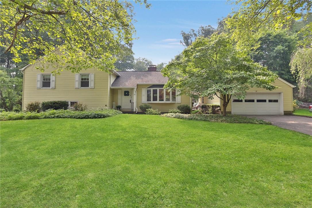 Pale yellow house with an attached garage, framed by mature trees above a broad green lawn.