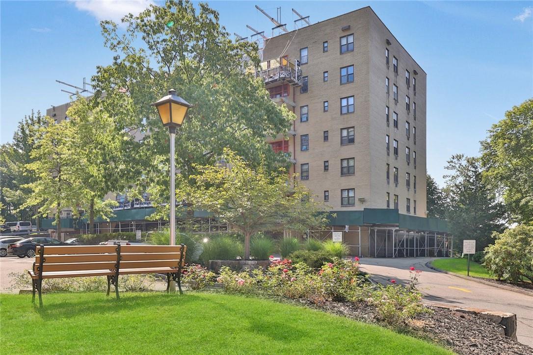 Tan brick apartment building with entrance scaffolding, a wooden bench, and landscaped grounds.