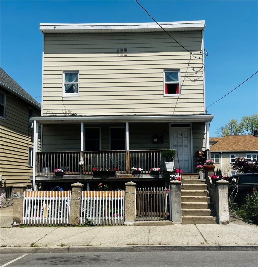 Two-story beige house with a covered porch, flower pots, and a fenced front yard.
