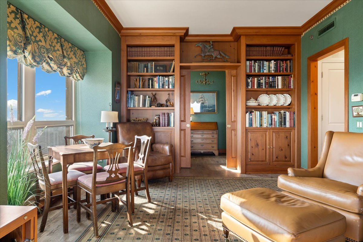 Living and dining room with wood built-in bookshelves, green walls, and tan leather seating.