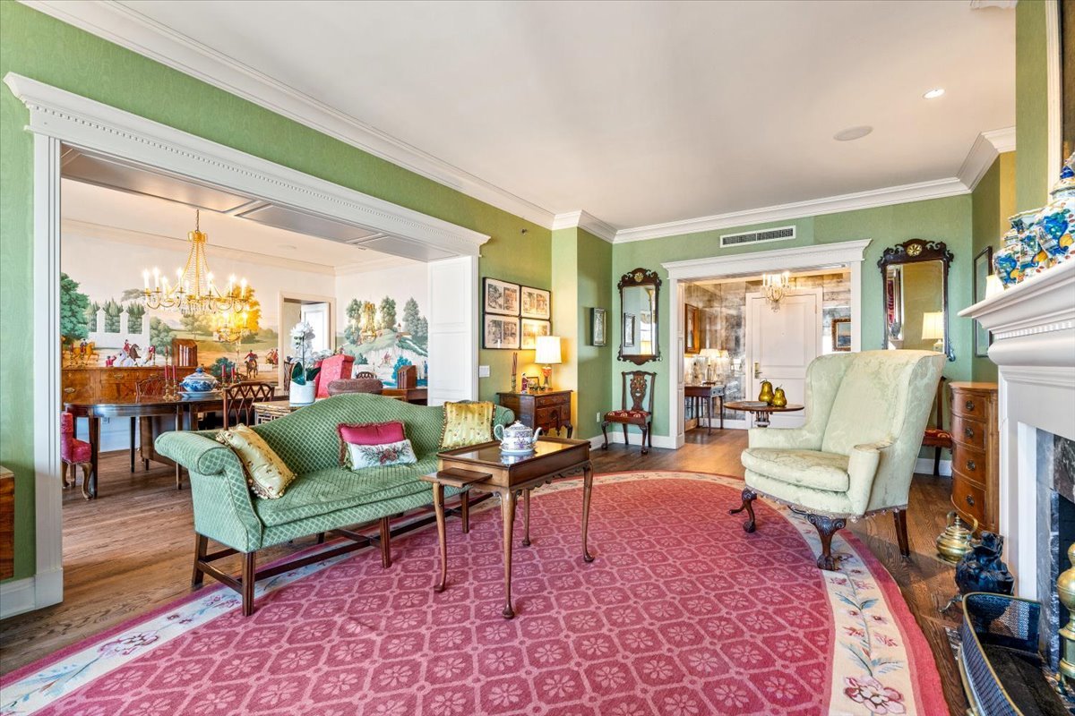 Furnished living room with a pink patterned rug, green sofa, fireplace, and mural in the adjoining dining area.