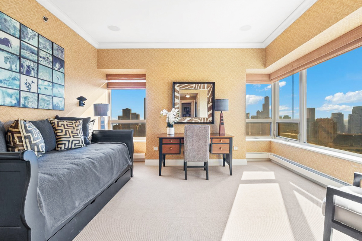 Furnished bedroom with a dark daybed, desk, and broad windows overlooking the Chicago skyline.