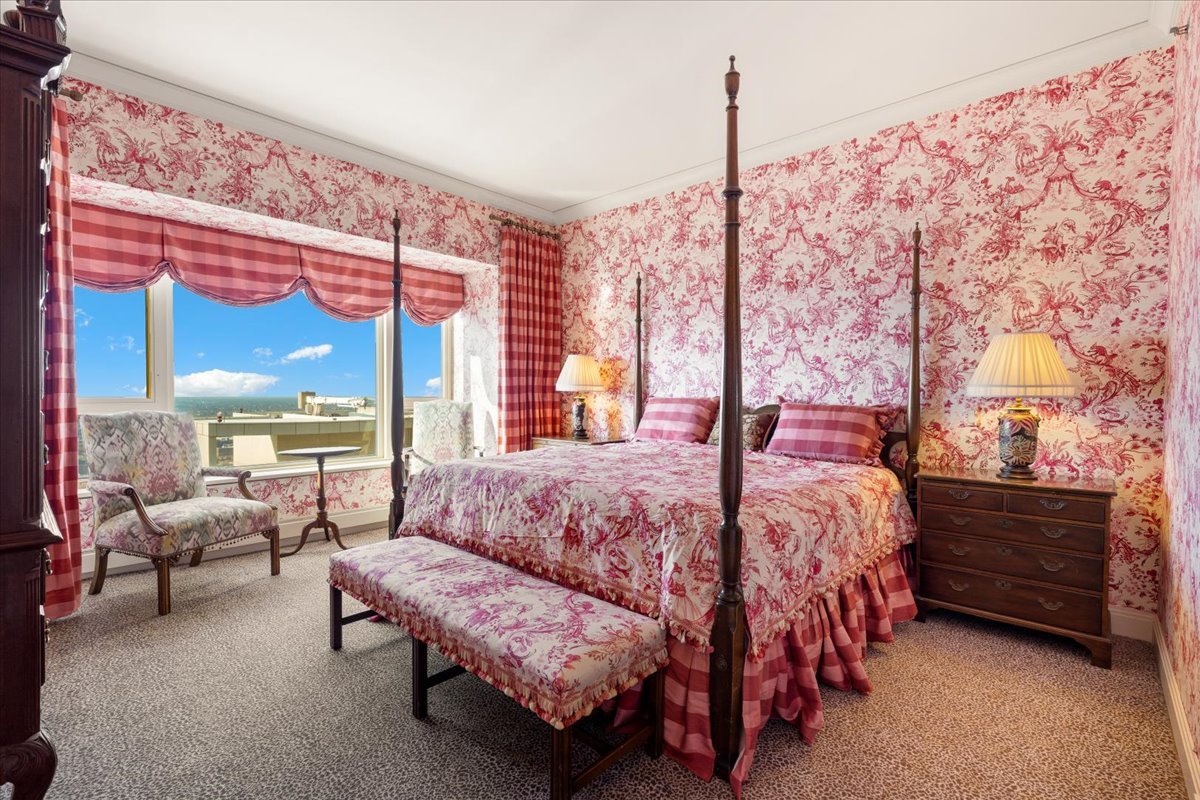 Bedroom with a four-poster bed, pink floral toile decor, and a large window overlooking the lake.