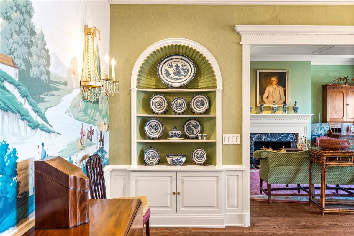 Furnished dining room with an arched china cabinet, landscape mural, and doorway to the living room.