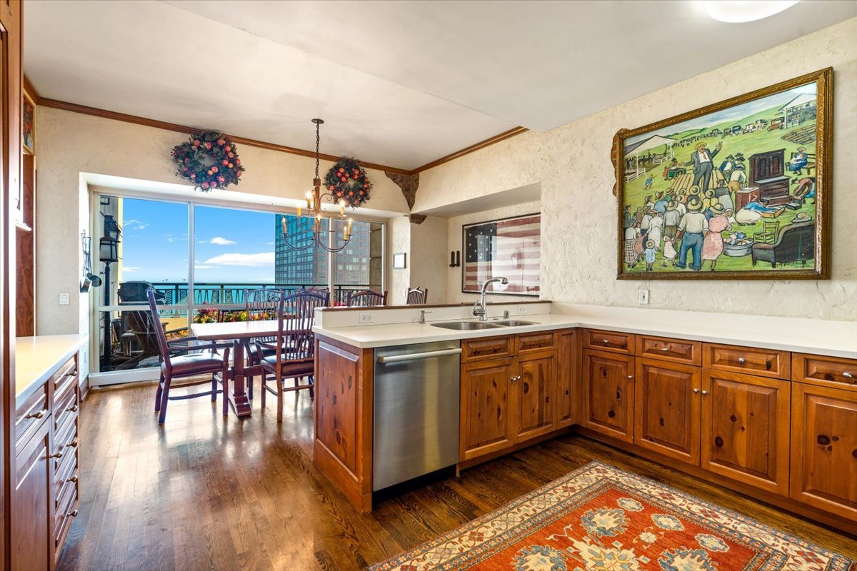Kitchen with warm wood cabinetry, stainless dishwasher, dining area, and lake views through sliding doors.