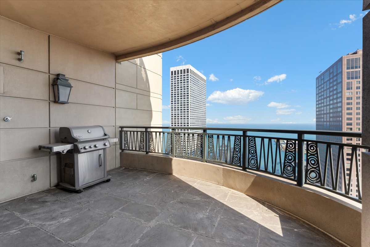 Stone-tiled balcony with a gas grill overlooking Lake Michigan and Chicago high-rises.