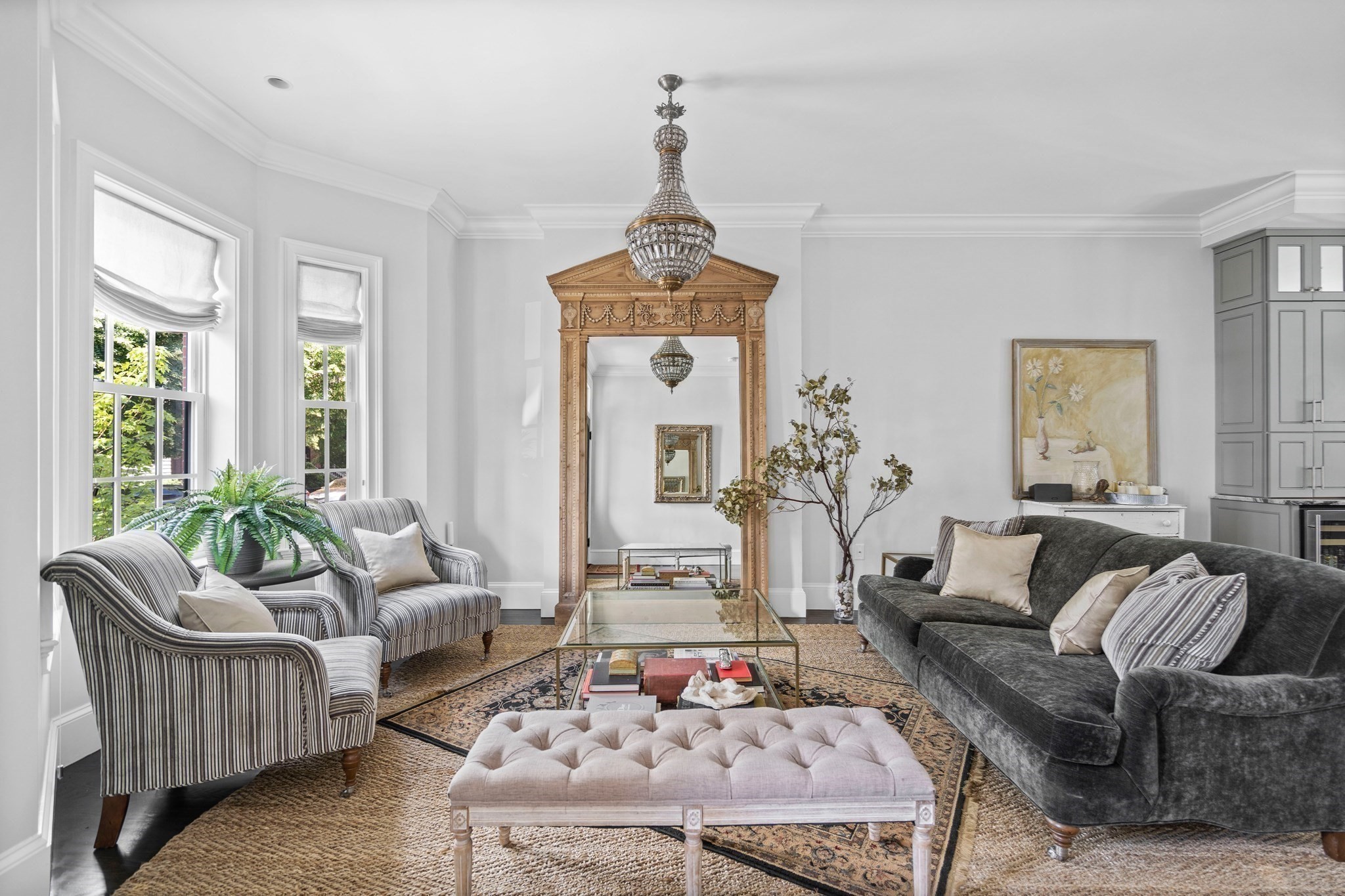 Living room with striped armchairs, dark sofa, tufted ottoman, and ornate gilt mirror.