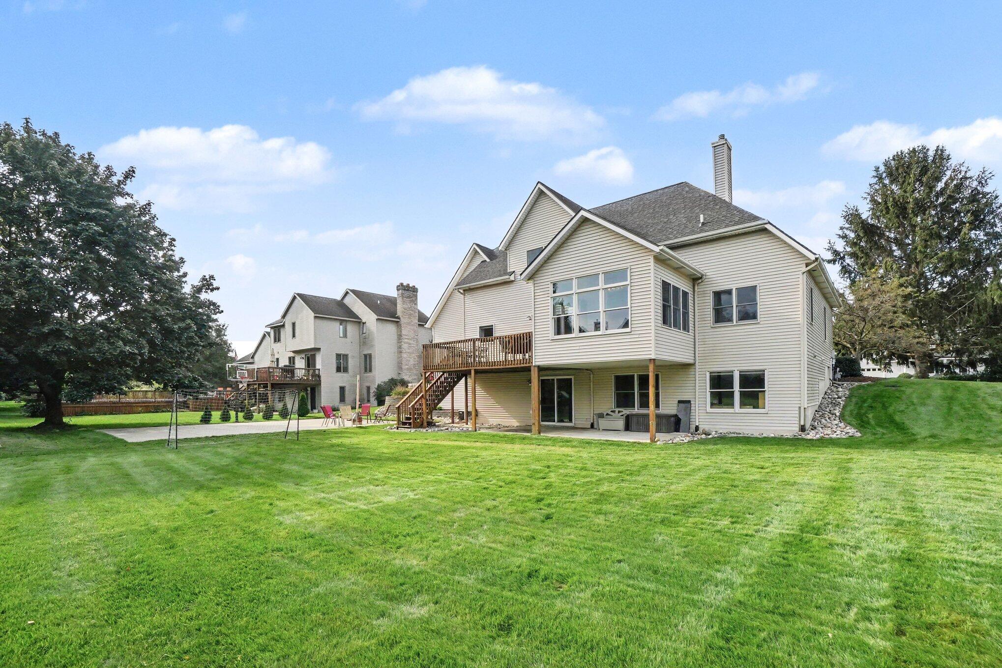 Rear of a two-story house with a raised deck, patio seating, and a broad green lawn.