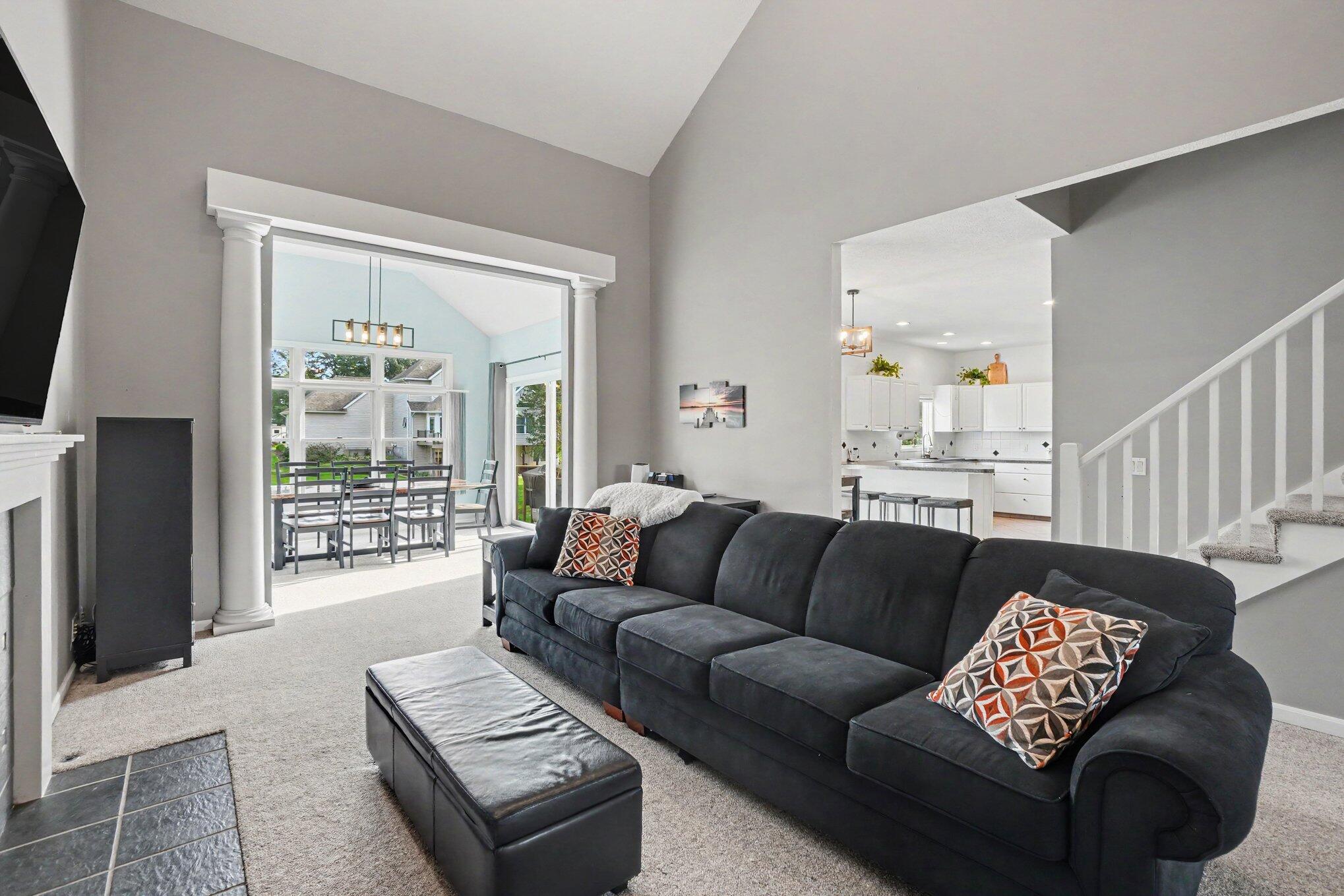 Living room with a dark sectional, opening to a bright dining area and white kitchen.
