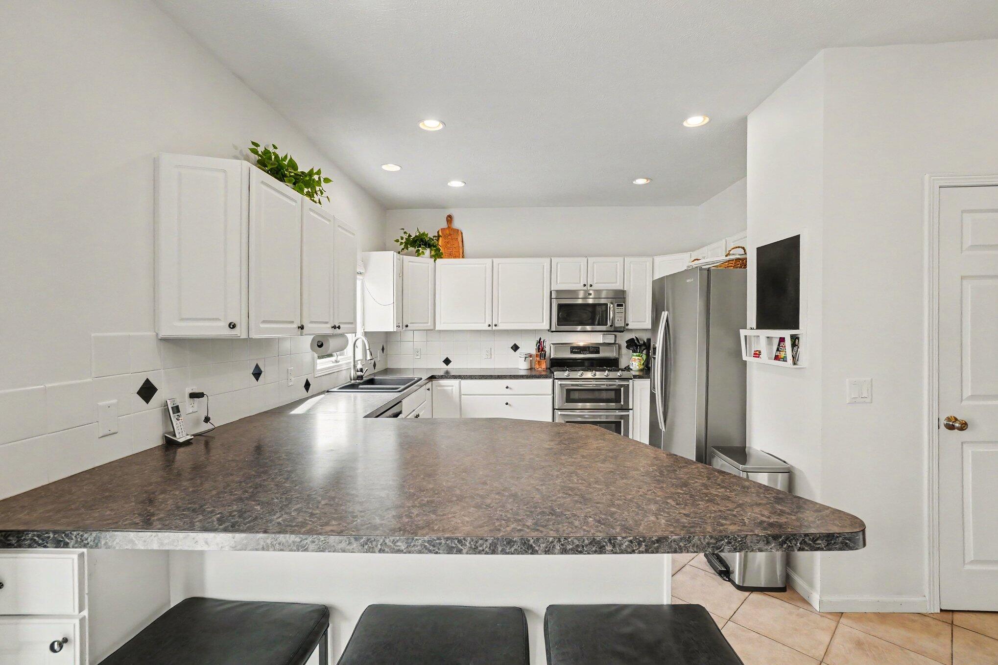 Kitchen with a large dark countertop peninsula, white cabinets, and stainless steel appliances.