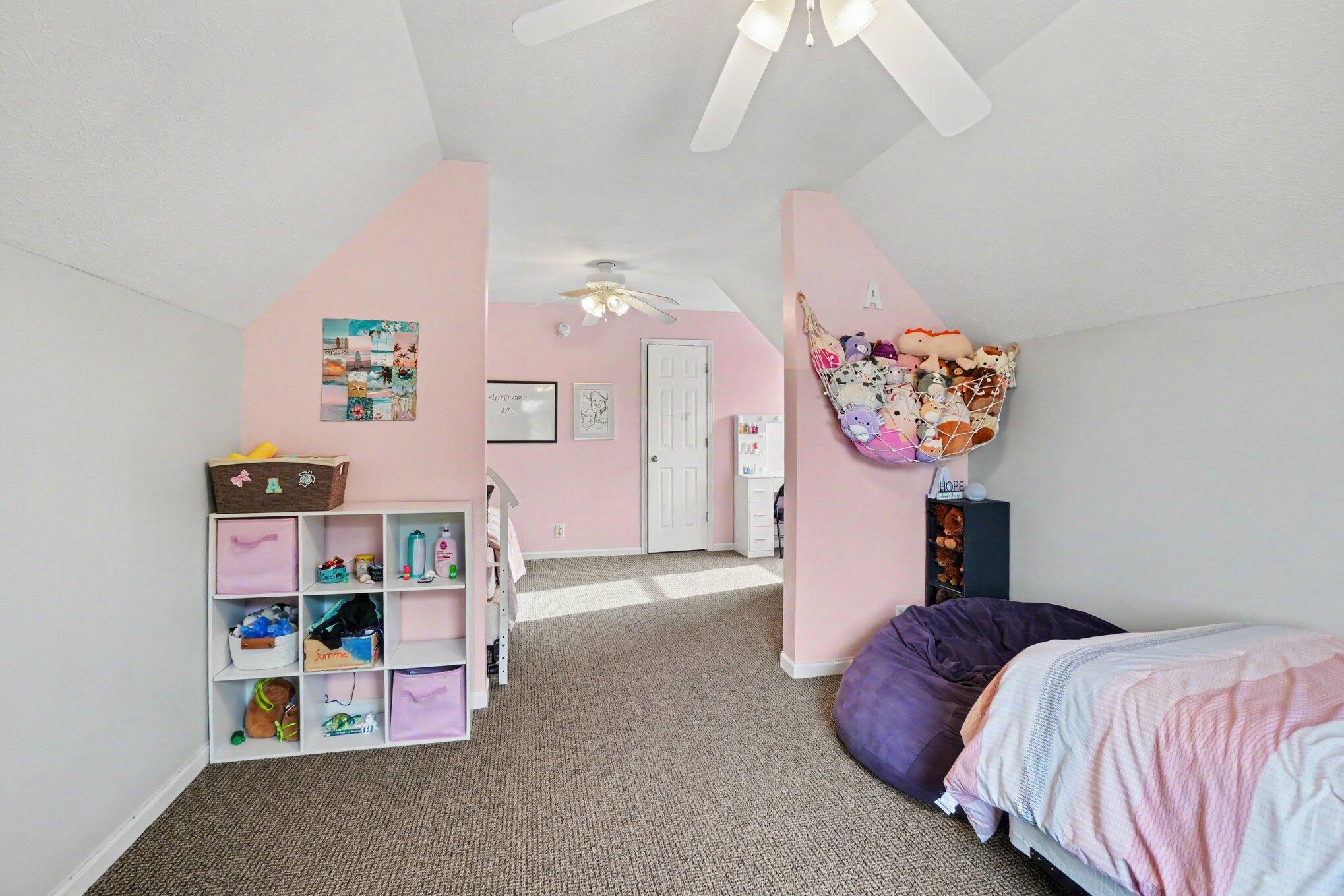 Pink children's bedroom with carpet, a bed, and stuffed animals in a wall hammock.