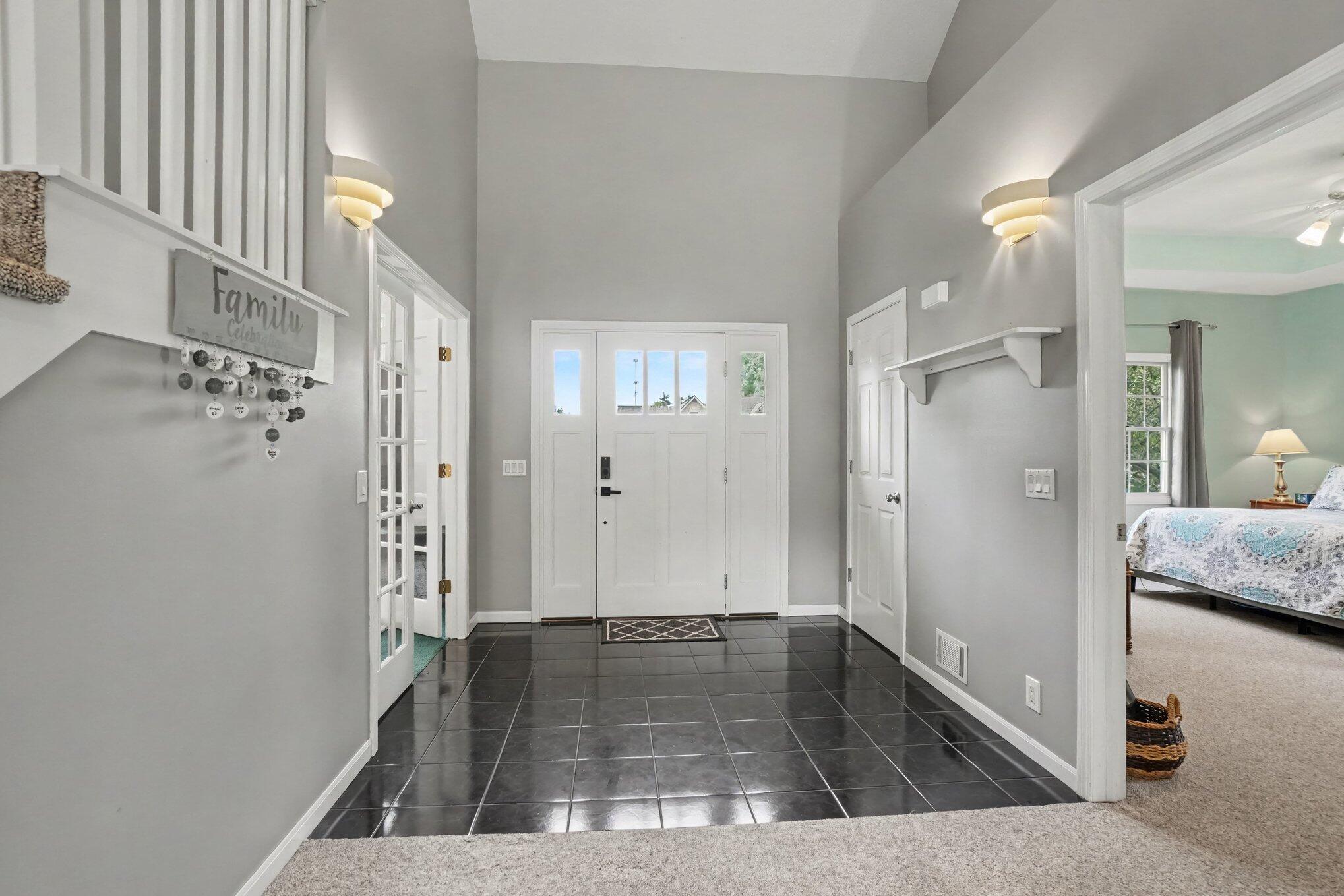 Entry foyer with glossy dark tile, a white paneled front door, and an adjoining bedroom.