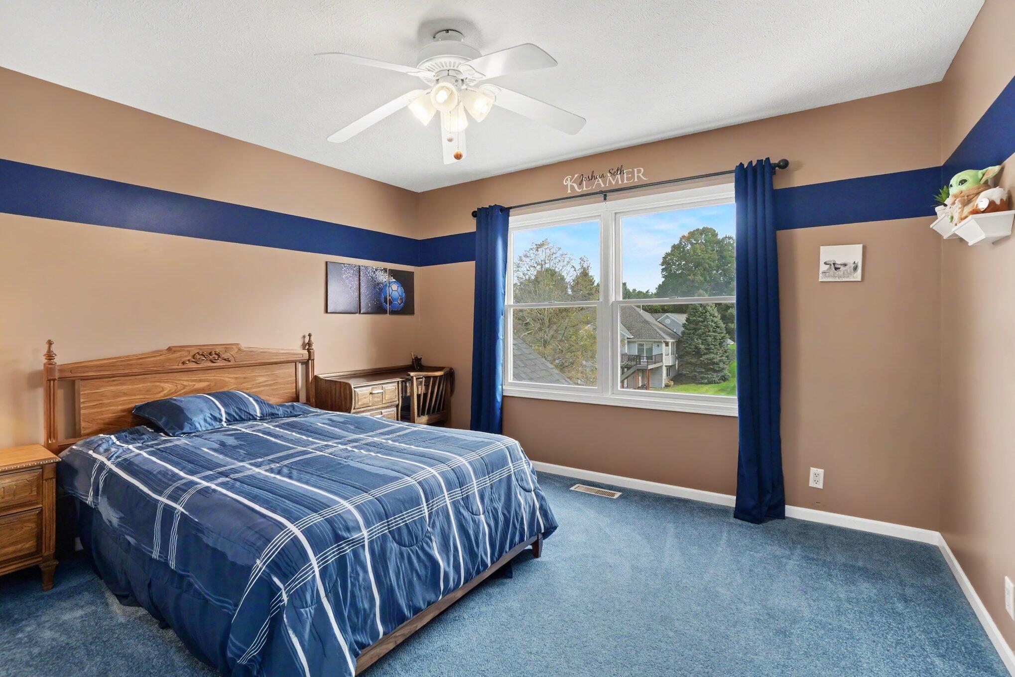Bedroom with blue plaid bedding, a wooden bed, and a large curtained window.