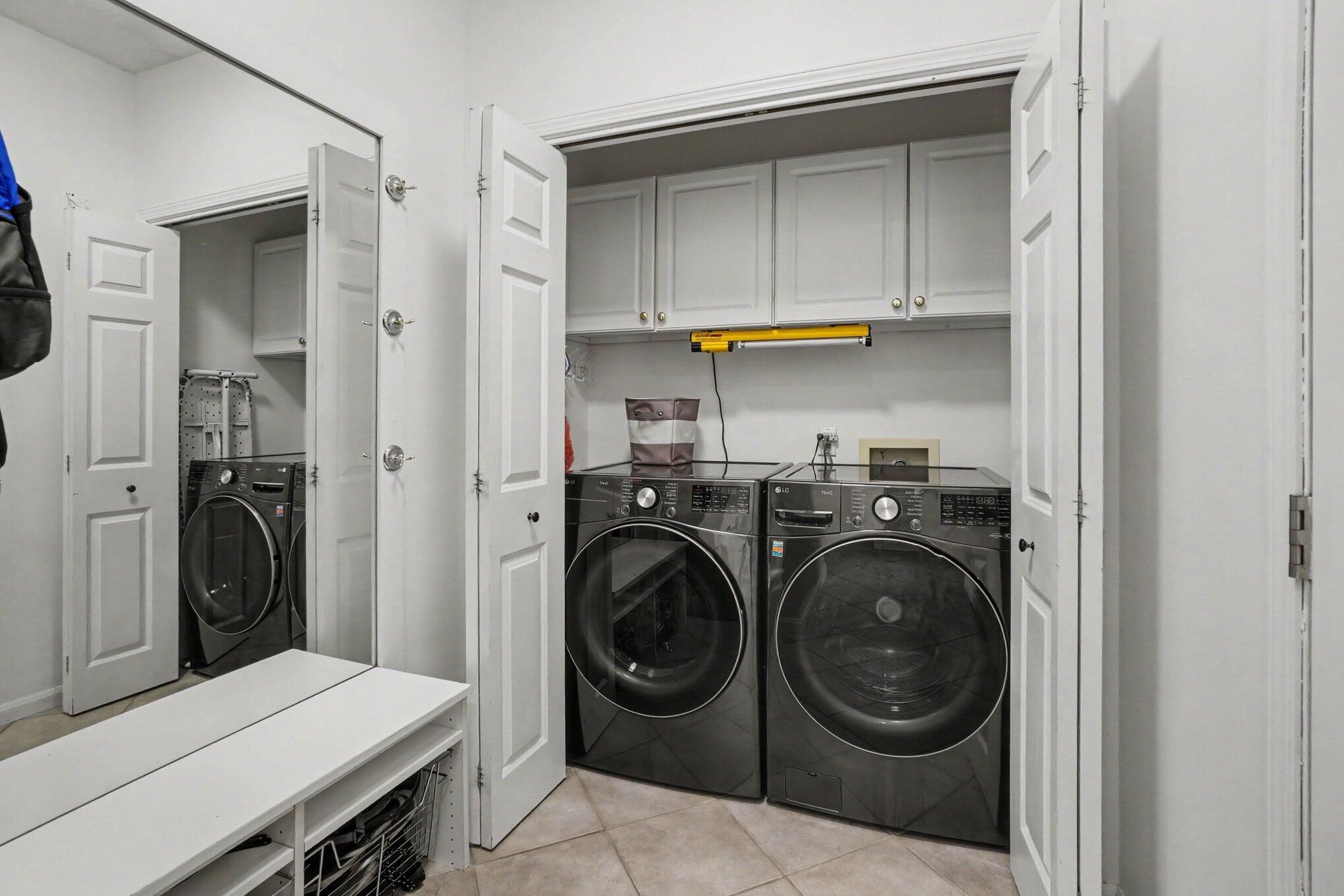 Laundry room with dark front-load washer and dryer beneath white cabinets, viewed through open paneled doors.