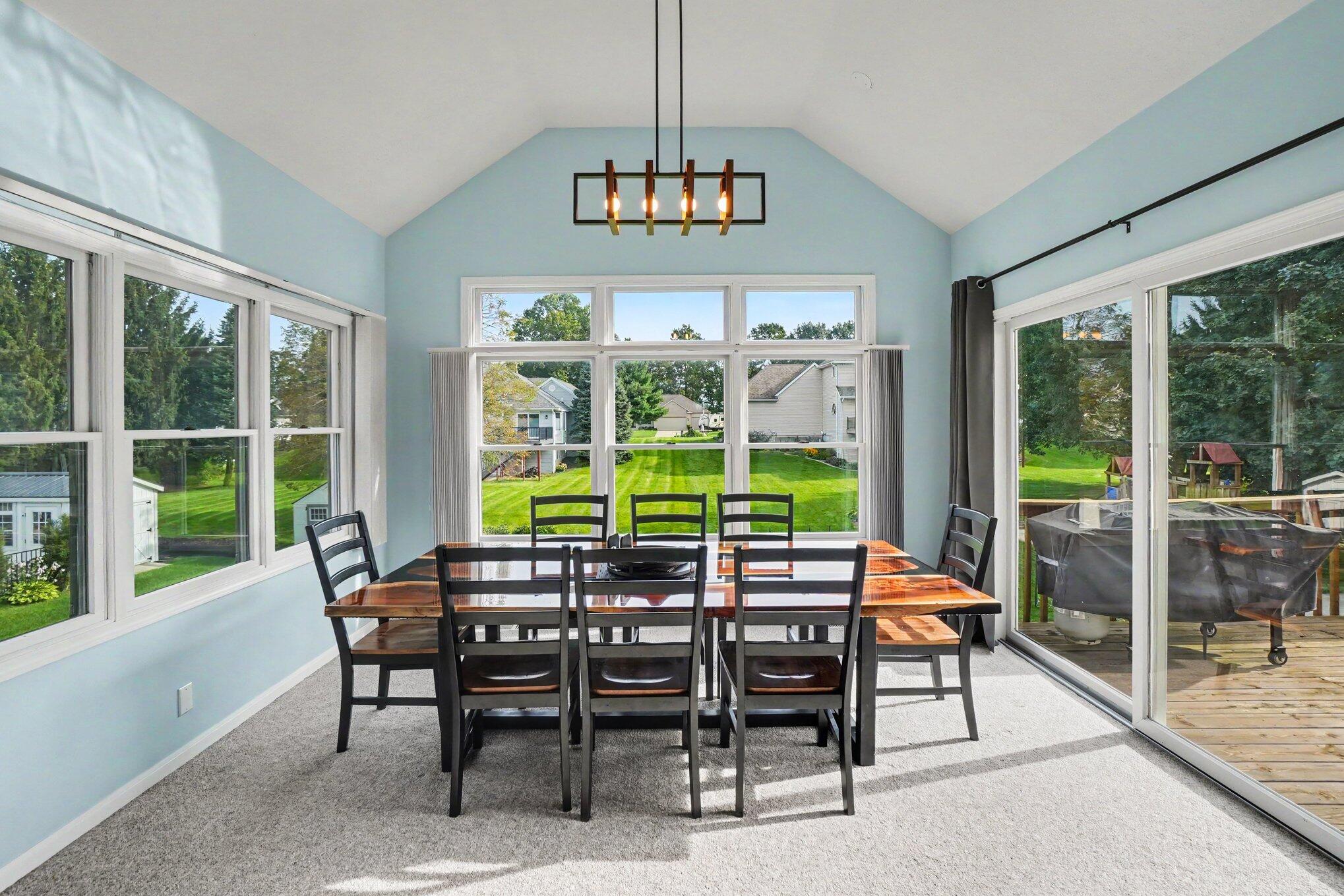 Dining room with vaulted ceiling, large windows, and sliding doors opening onto a deck.